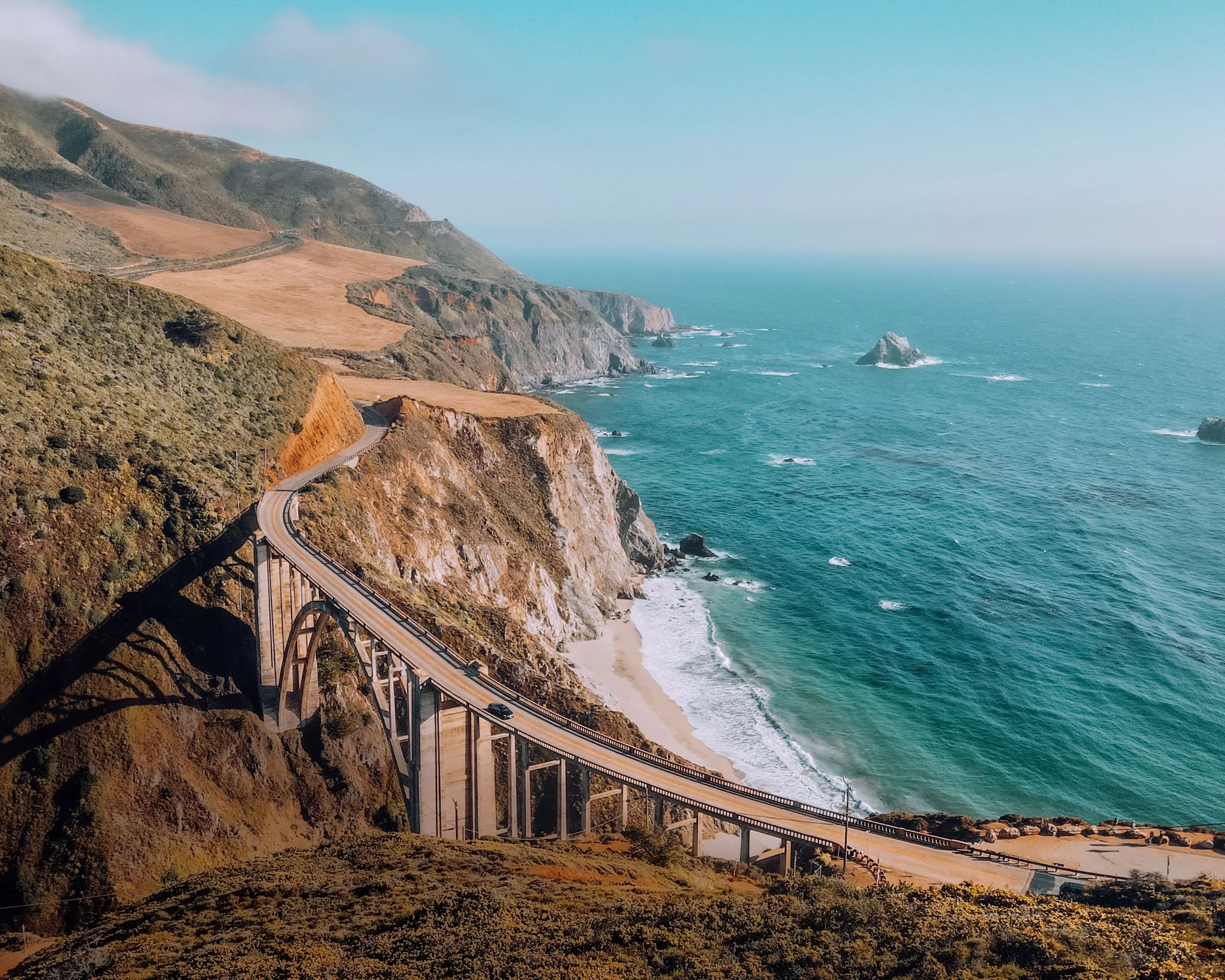 A car crossing Bixby Creek Bridge on California’s coastal highway, with cliffs and turquoise Pacific water below.