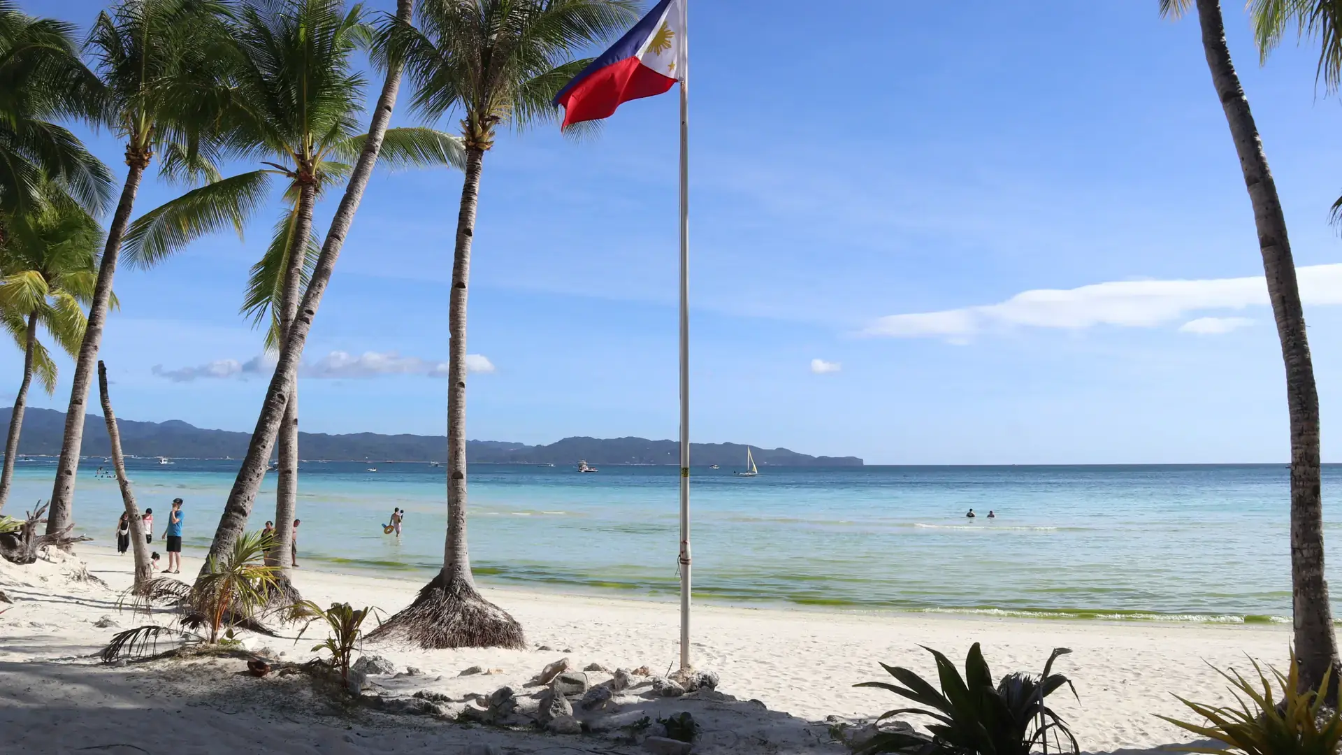 Powder-white sand, leaning palms and a Philippine flag on Boracay's White Beach under a blue sky