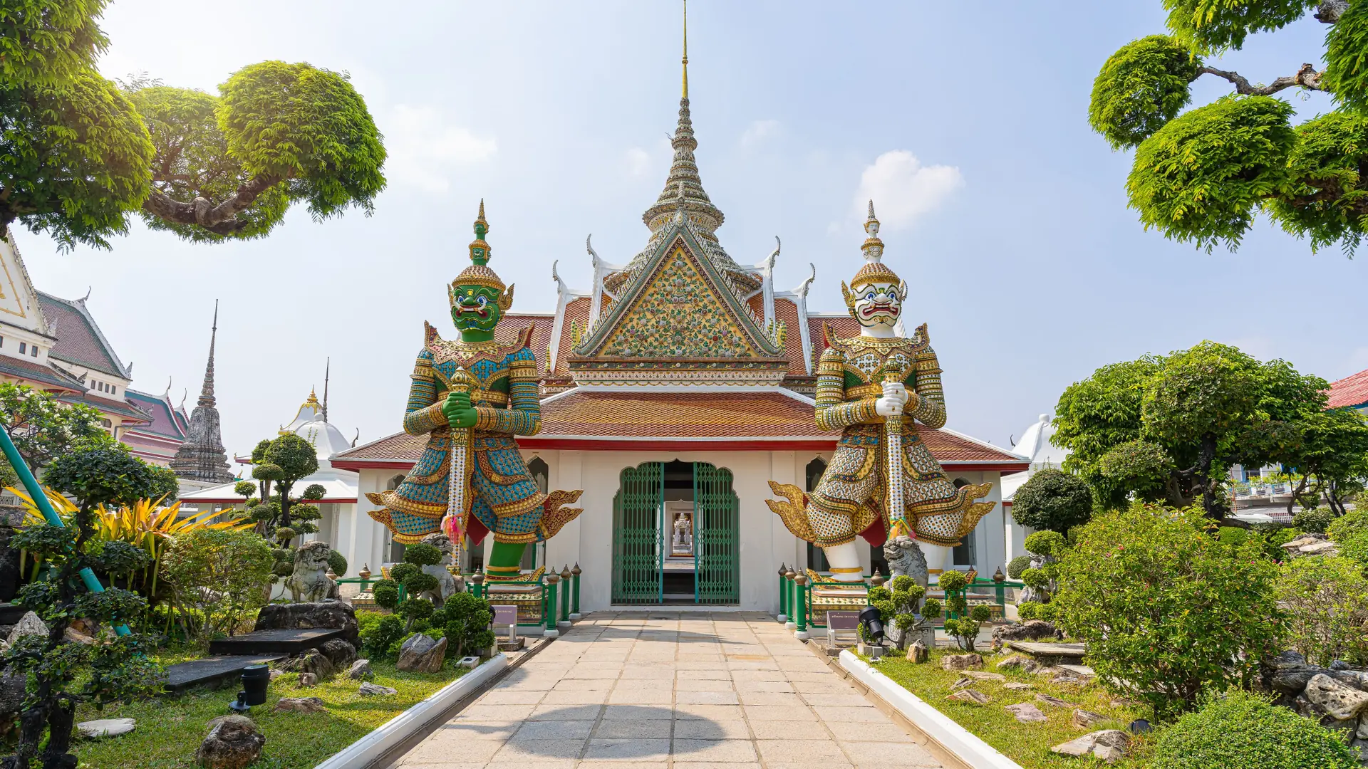 Stone guardian figures standing below the ornate roof of Wat Arun in Bangkok