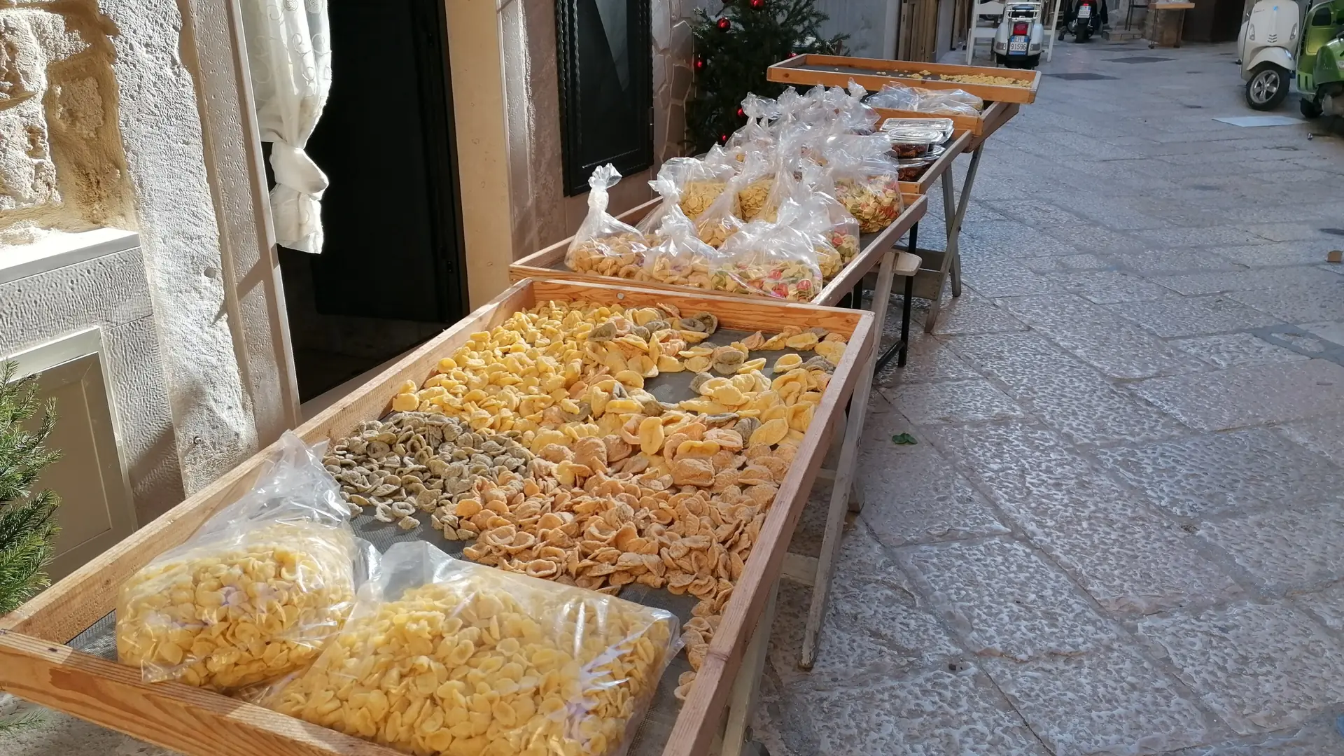 fresh orecchiette pasta drying on trays in a sunlit Bari Vecchia street