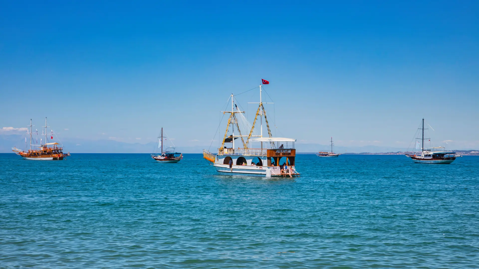 Boats crossing clear blue Mediterranean water off Side under a bright summer sky