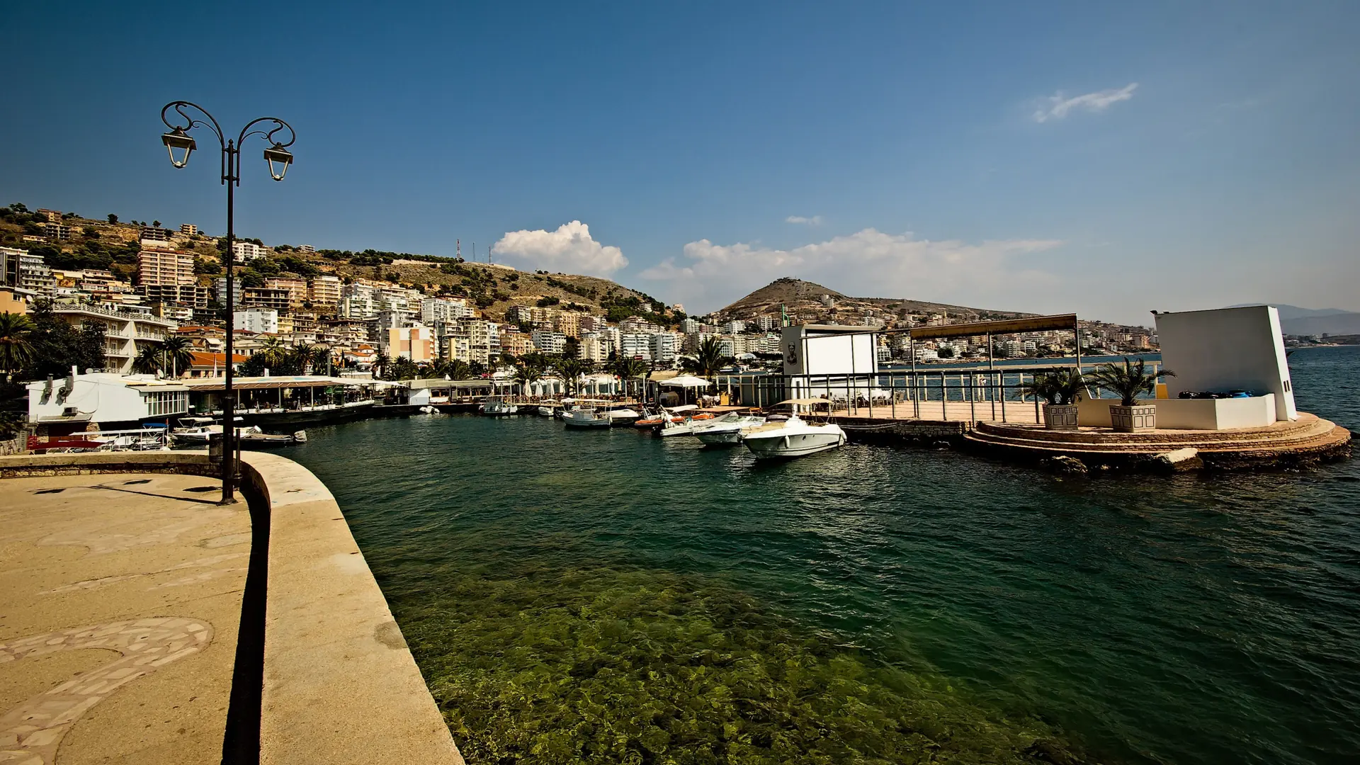 Lamp posts, moored boats and the waterfront of central Sarandë under a deep blue sky