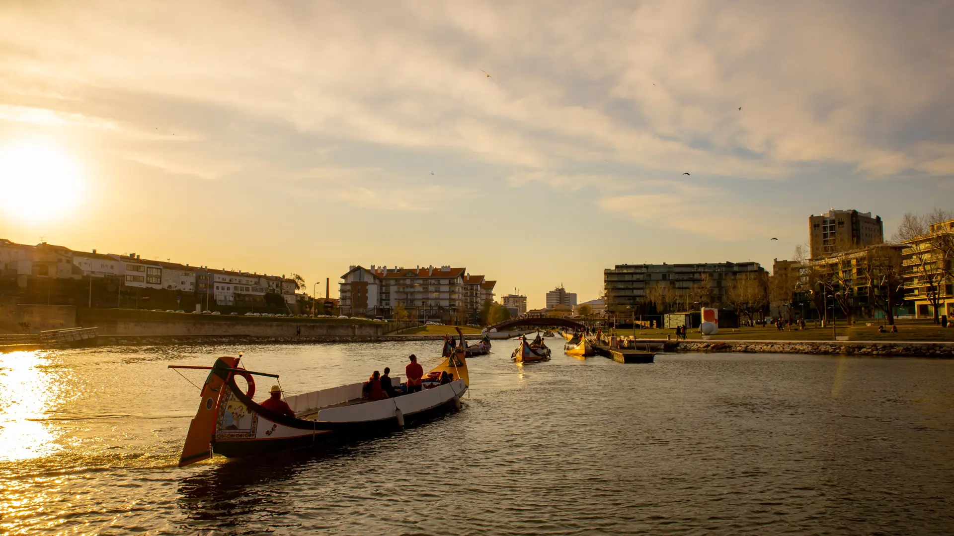 Traditional boats crossing Aveiro’s lagoon at sunset with the city beyond