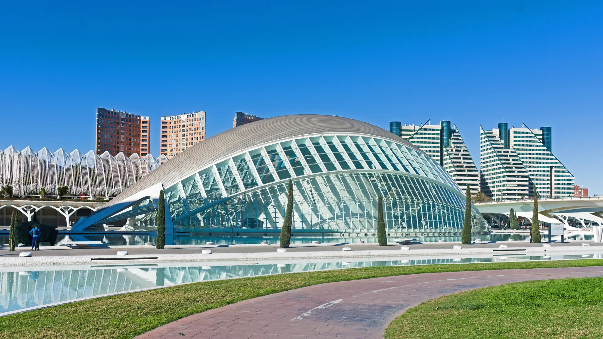 Sunlit Hemisfèric glass ribs and curved shell beside a reflecting pool at Valencia’s City of Arts and Sciences.