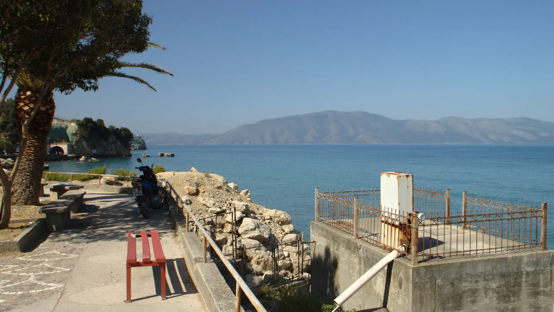 A seaside walkway above the Bay of Vlorë with the Karaburun peninsula across the water on a sunny day