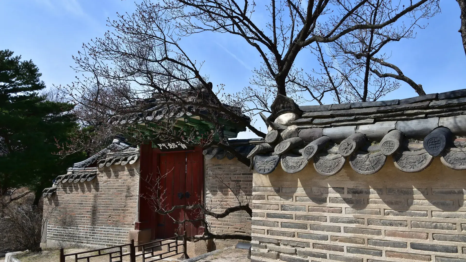 A traditional red gate and tiled wall at Changdeokgung Palace under a bright blue sky in Seoul