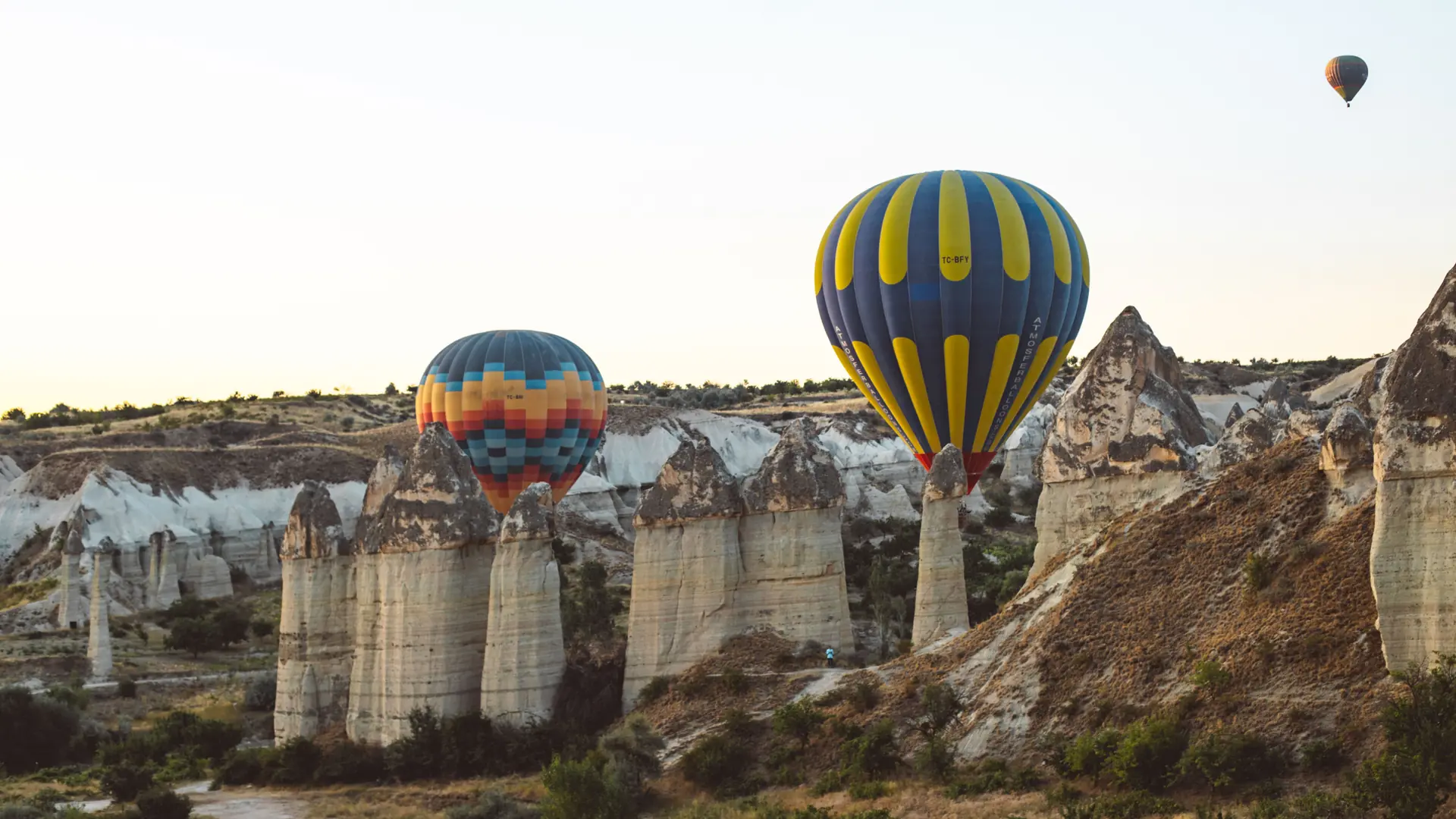 Hot-air balloons floating above Göreme fairy chimneys and sunlit Cappadocia valleys at sunrise