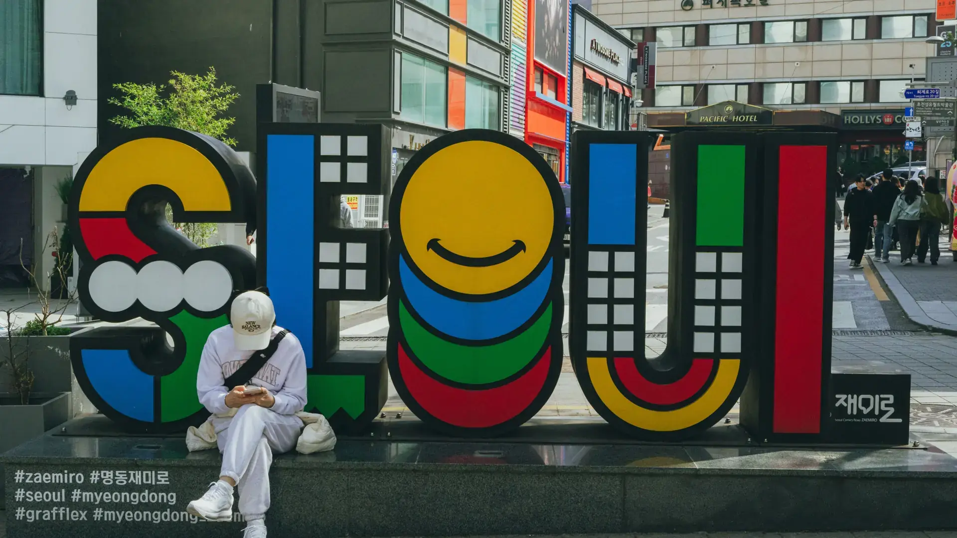A colorful 'SEOUL' sign sculpture on a sunny Myeongdong street corner