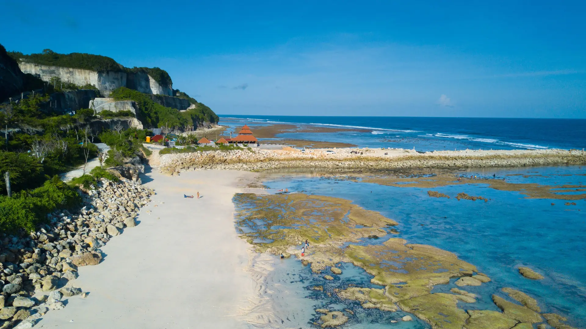 White sand, limestone cliffs and shallow coastal pools at Melasti beach in Ungasan beneath a clear blue sky