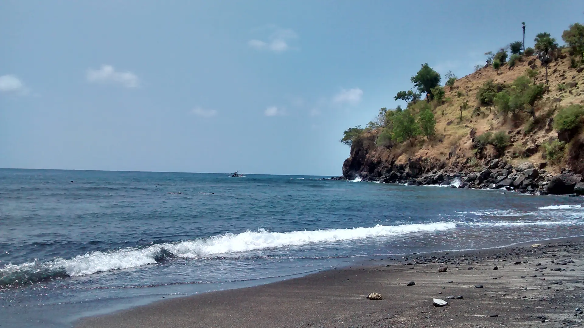 Dark shoreline, blue water and a rocky headland at Jemeluk Bay on the Amed coast