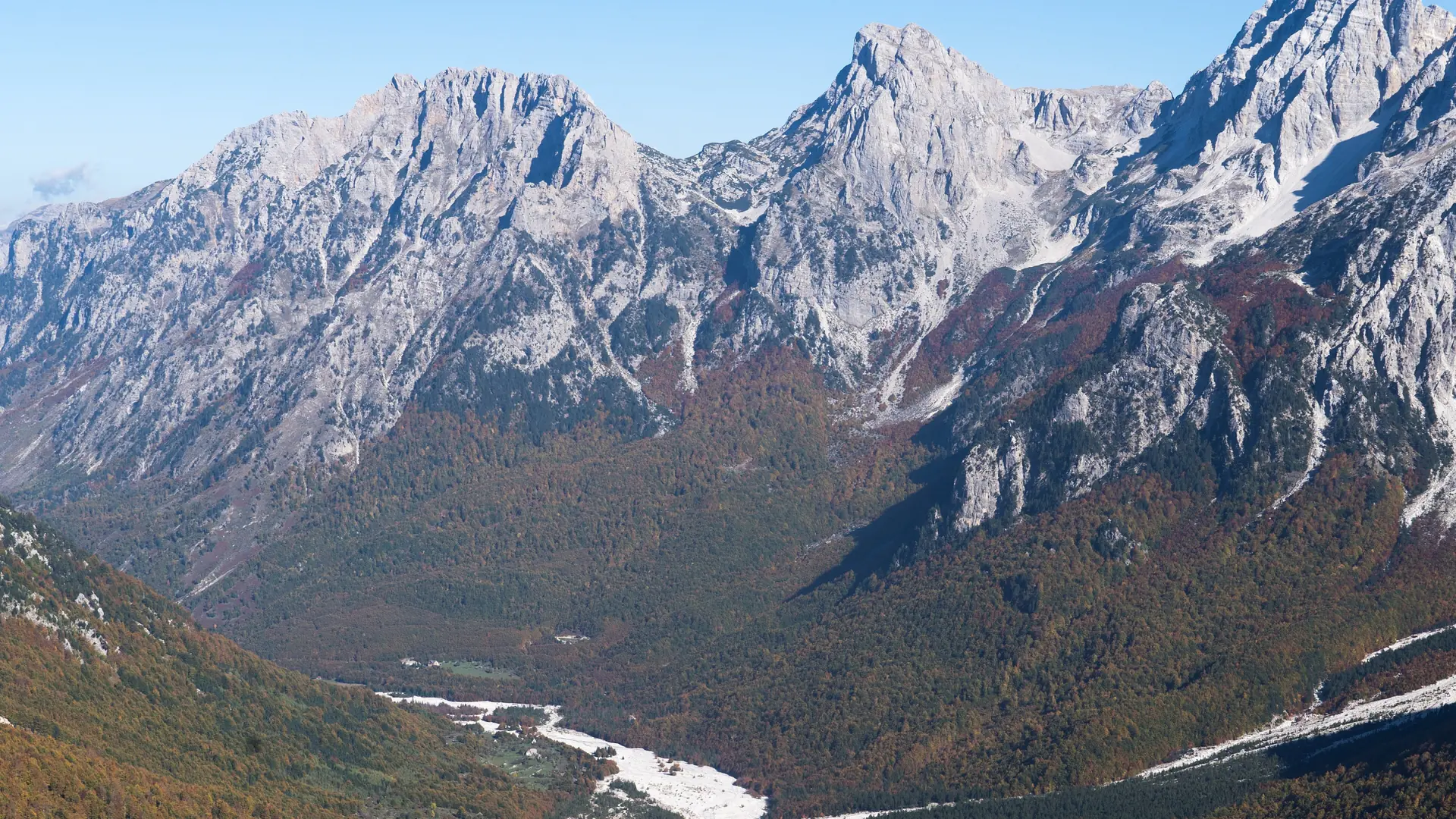 Grey limestone peaks above the forested Valbona valley and its wide riverbed on a clear day