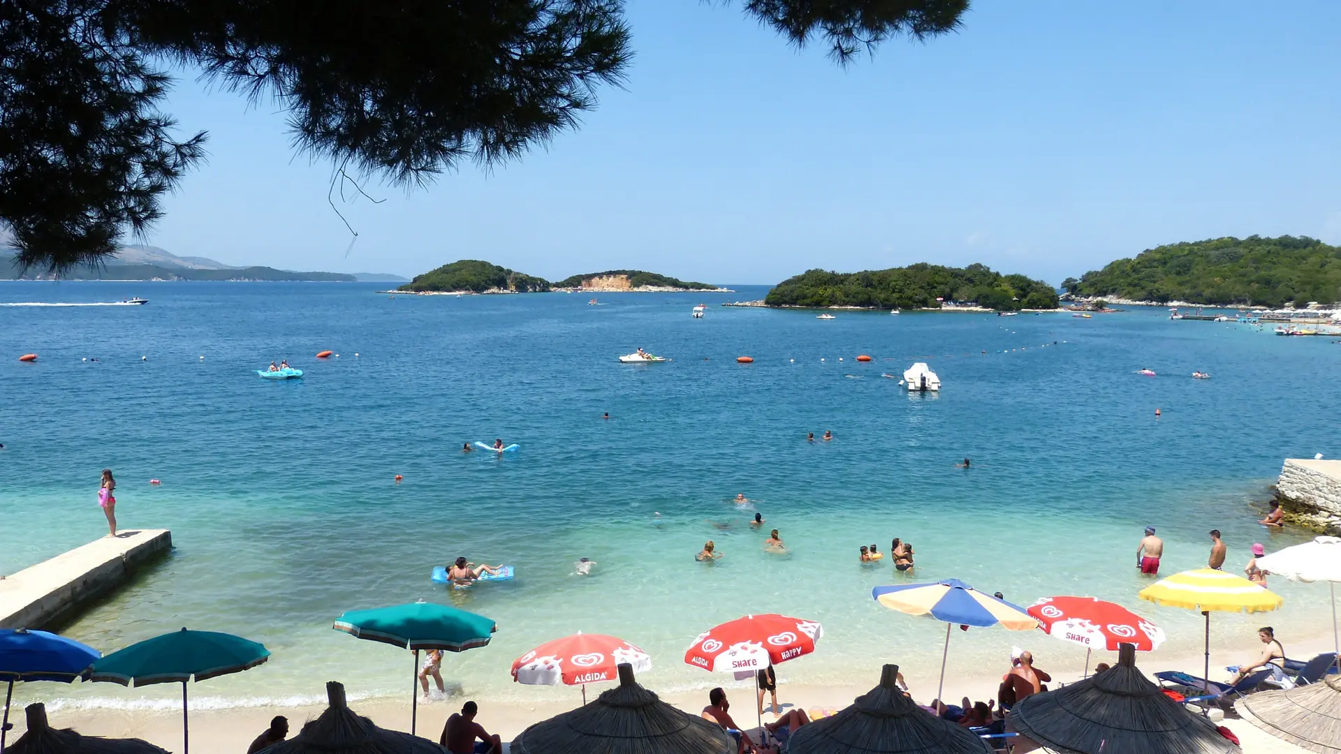 Umbrellas on a Ksamil beach facing the wooded Ksamil islets across clear turquoise water on a bright summer day