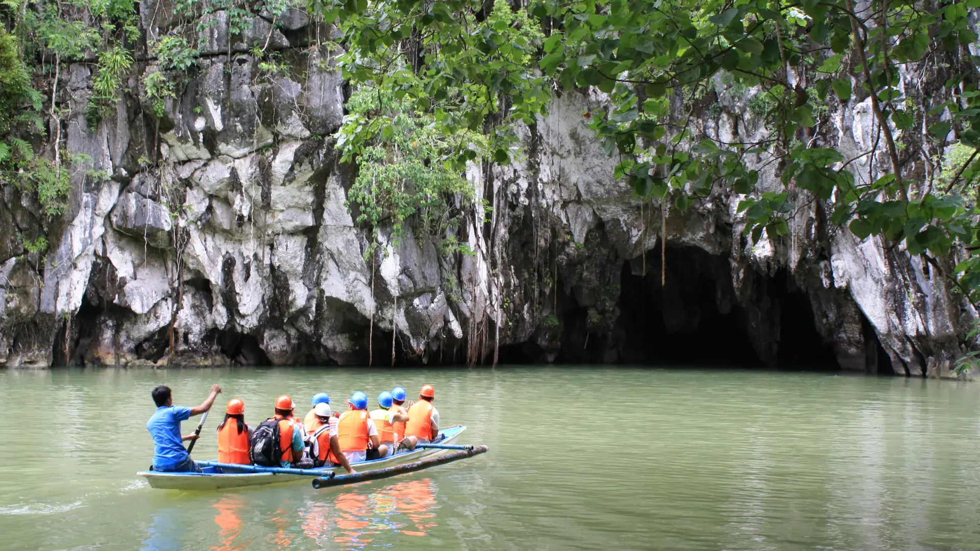 Tourists in orange life vests paddling into the limestone mouth of the Puerto Princesa Underground River