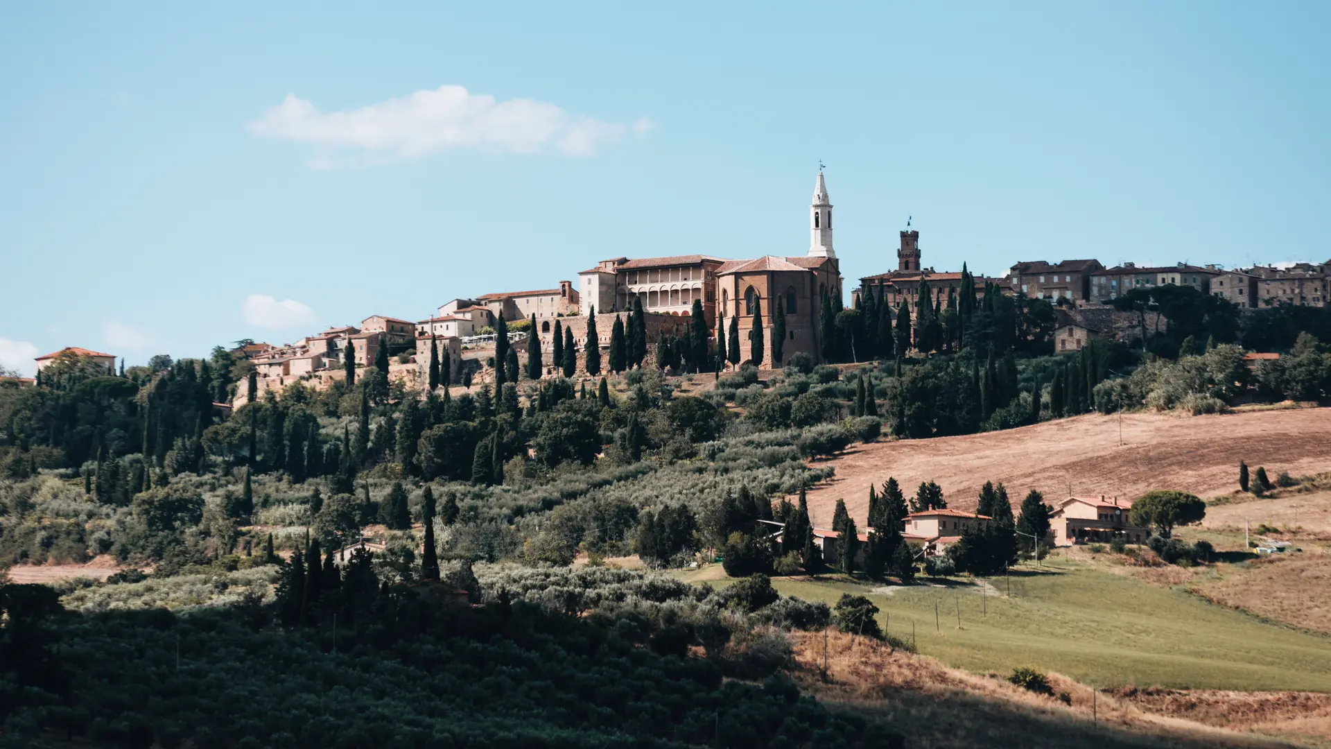 Pienza’s cathedral and Palazzo Piccolomini above the Val d’Orcia hills in daylight.