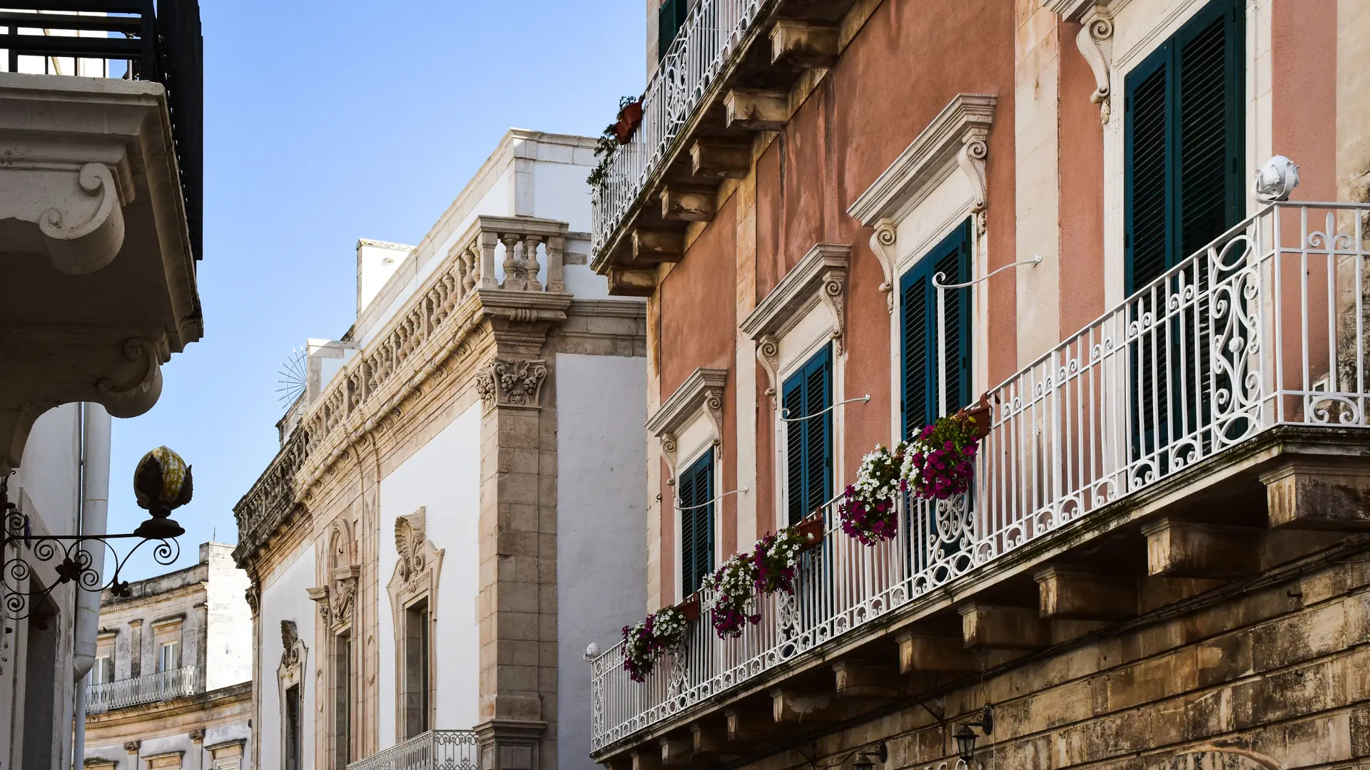 baroque stone balconies with flowering plants on a sunlit Palermo facade