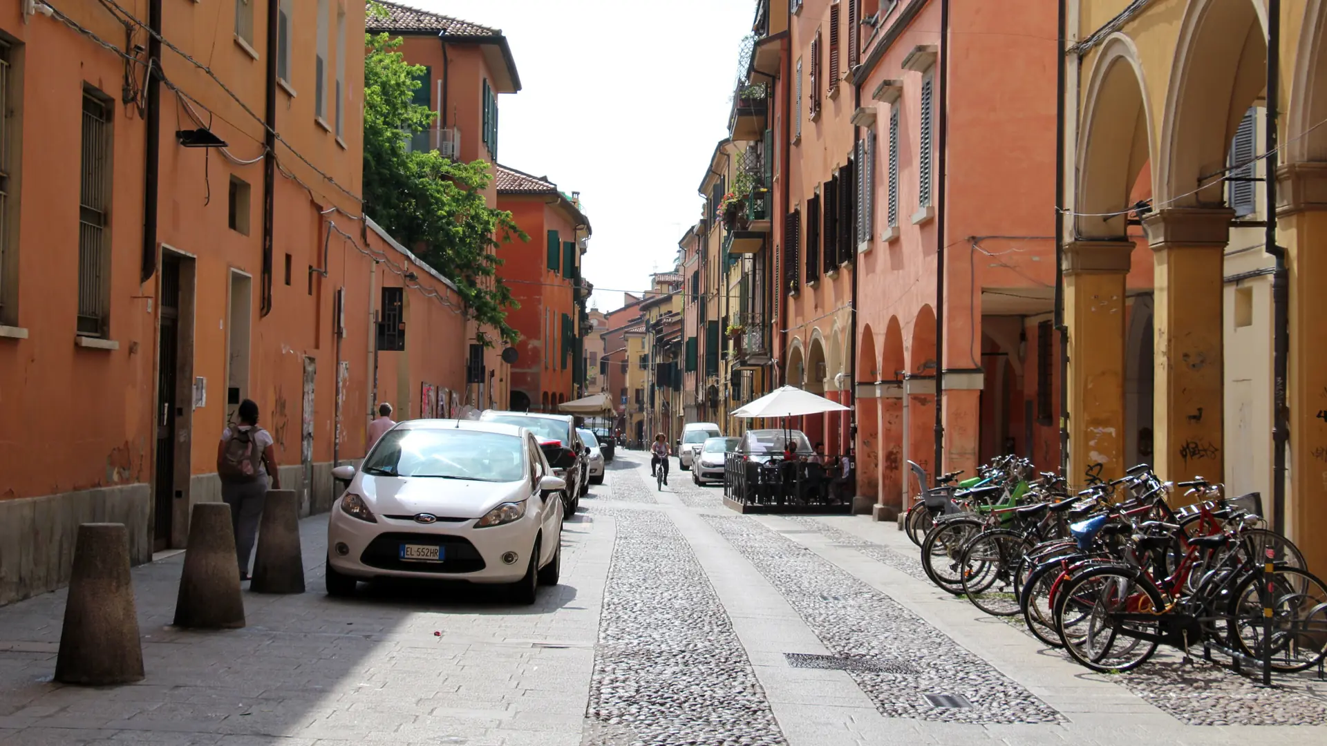 golden-hour Pratello street in Bologna with porticos, small trattoria terraces and bicycles