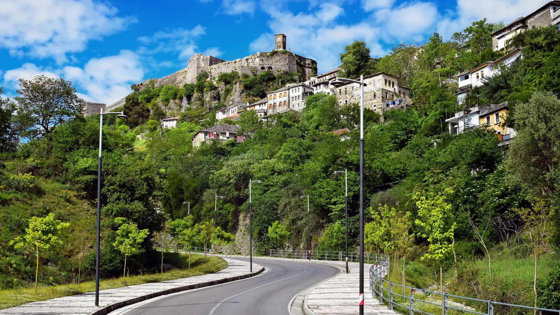 Gjirokastër Castle above the stone houses of the old town, with green slopes under a bright blue sky