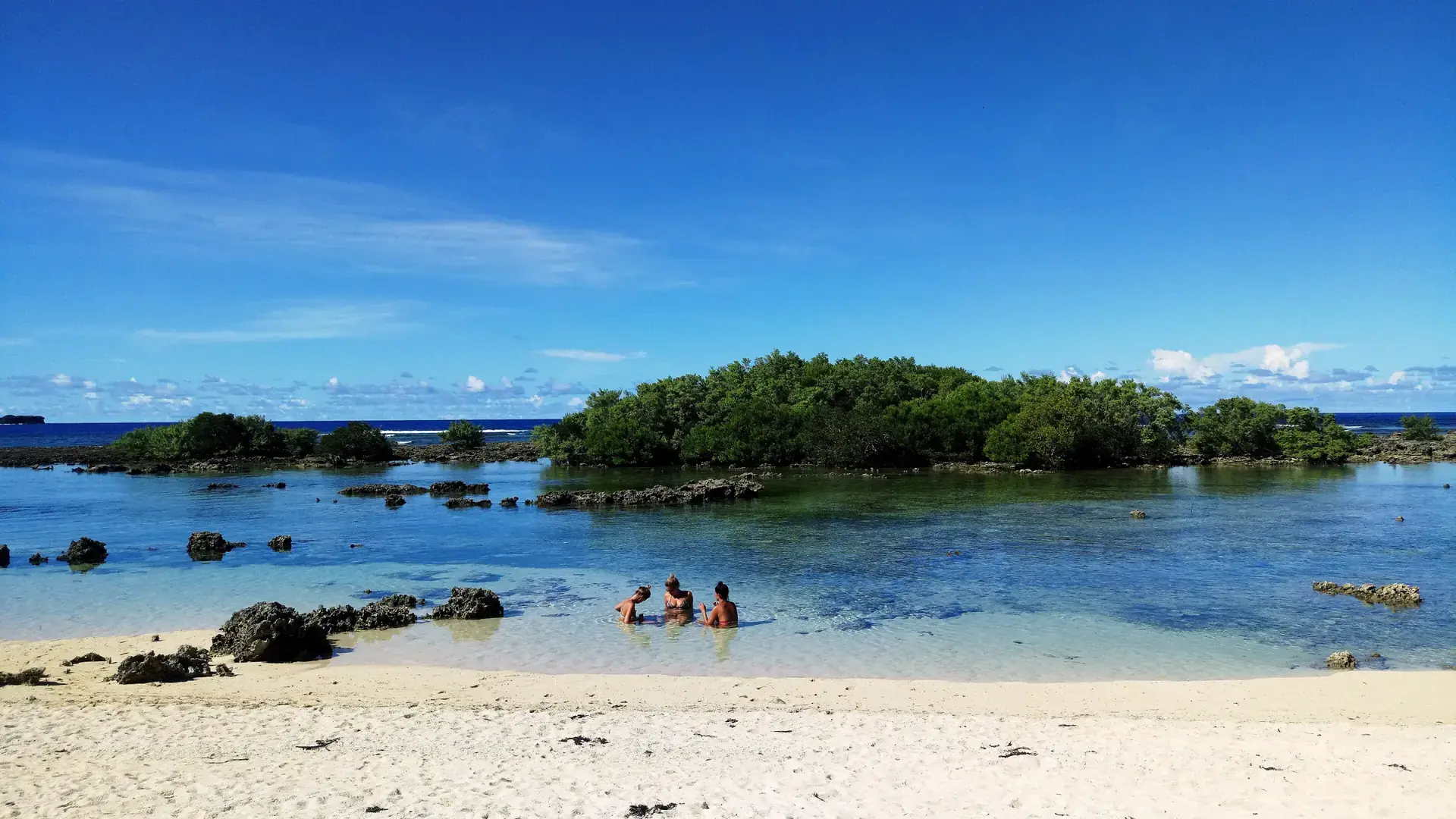 Swimmers in shallow water beside a rocky, sandy shore on Siargao
