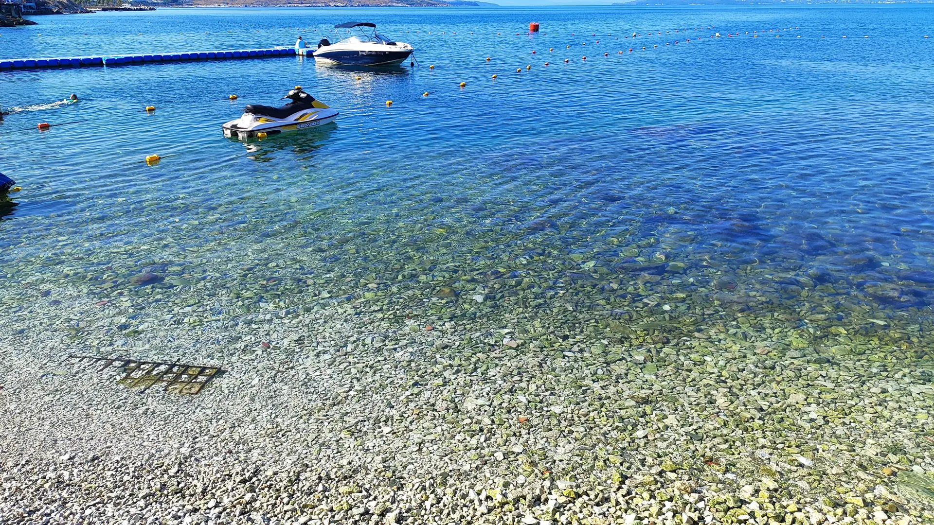 Clear turquoise shallows and moored boats off a beach near Bougainville Bay on Sarandë's Butrint road