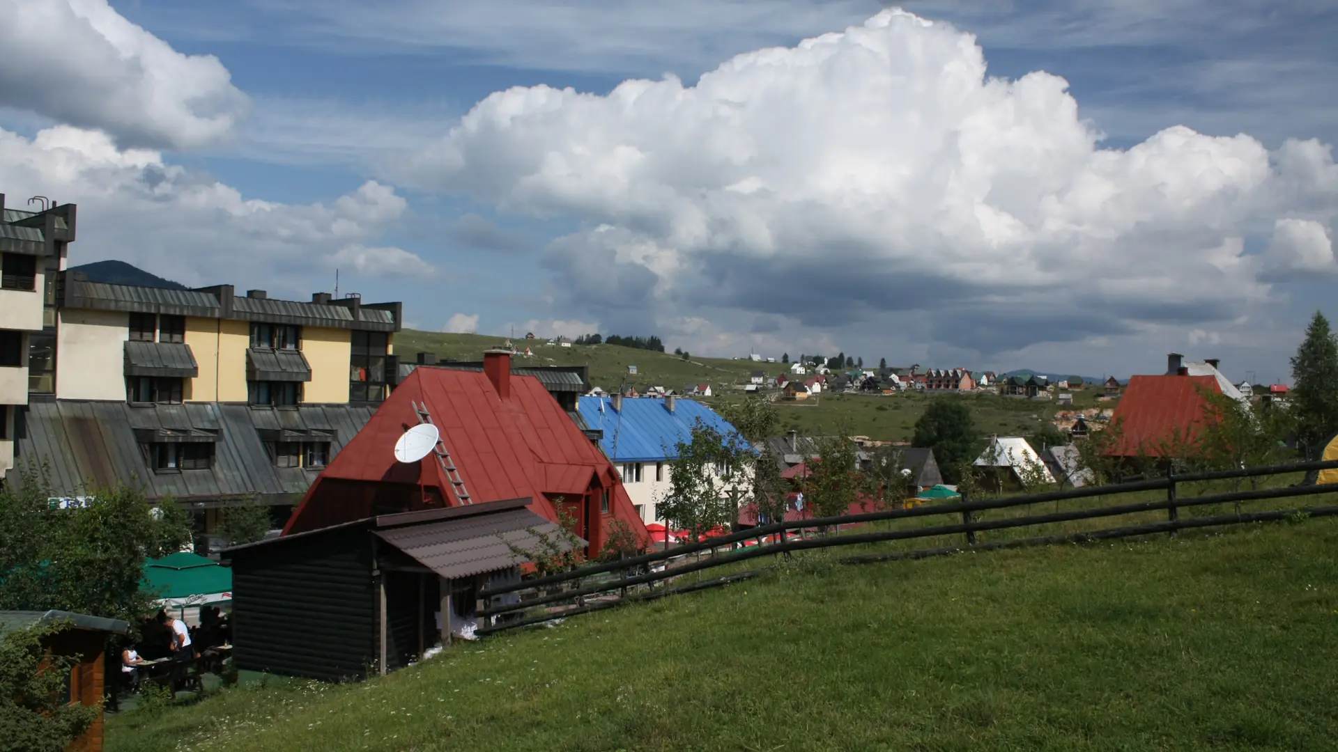 Žabljak town centre houses and meadow beneath a blue, cloud-filled sky