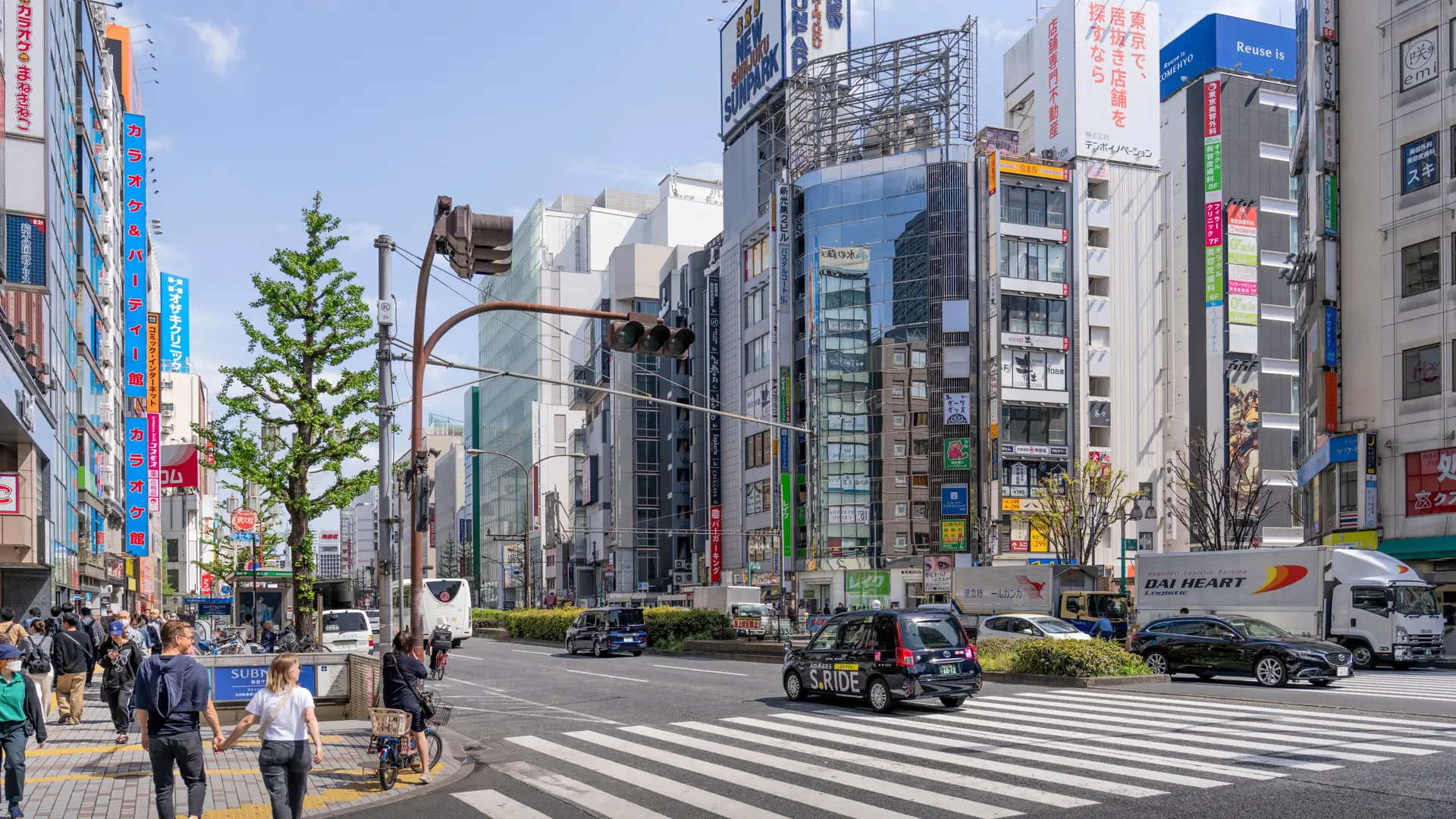 Shop signs and pedestrians at a sunny crossing in Shinjuku, Tokyo