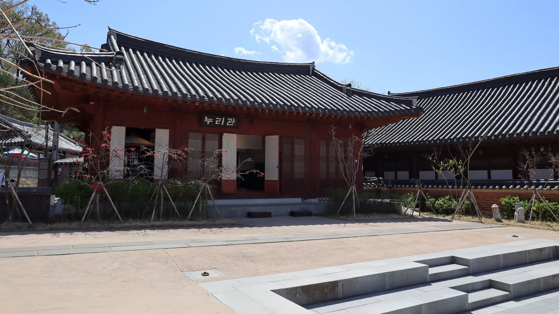 A traditional hanok building in Jeonju Hanok Village with a Korean sign above its doorway, under a clear blue sky with flowering trees