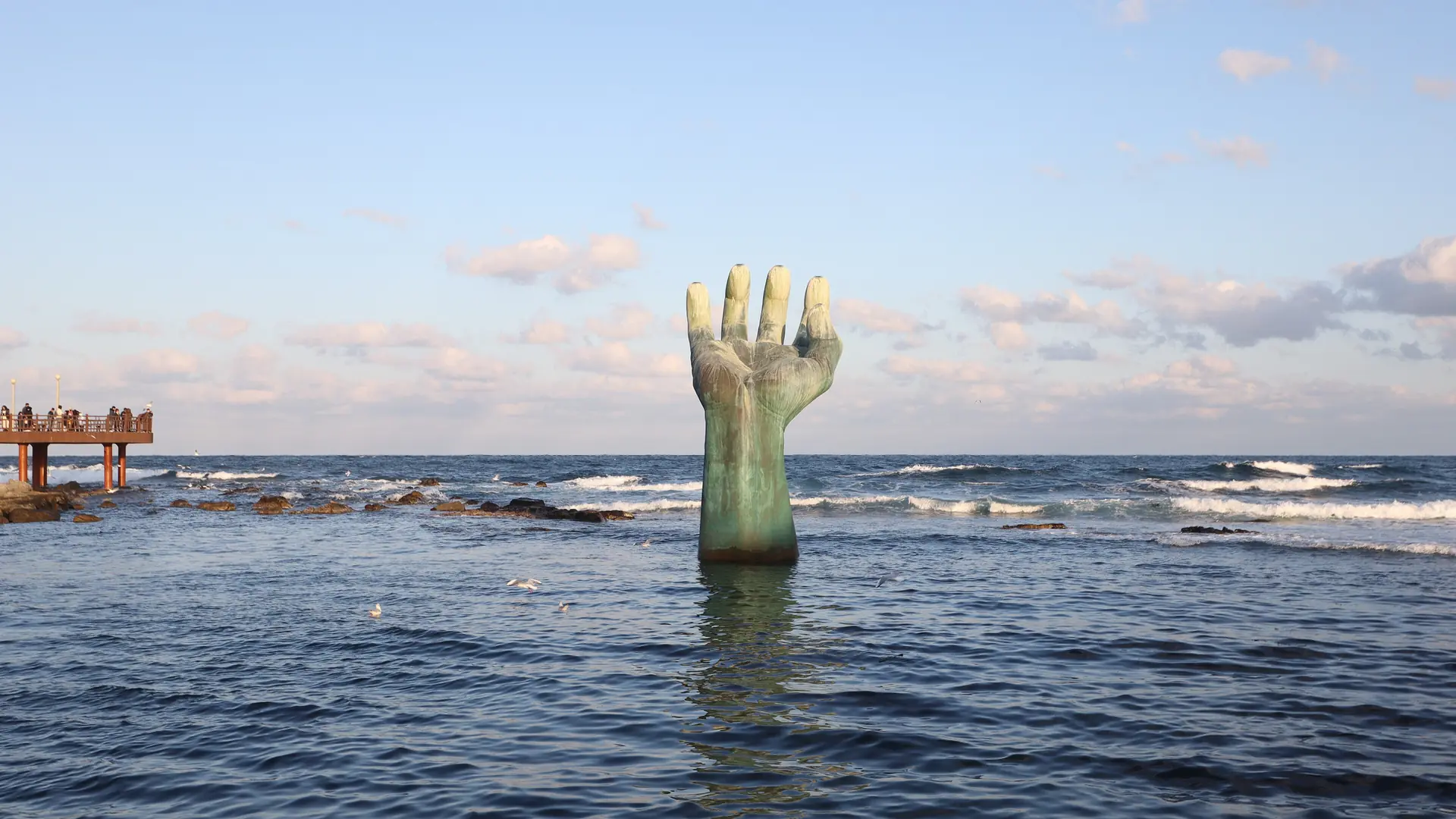 The bronze Hand of Harmony rising from the sea at Homigot, Pohang, with waves around its base