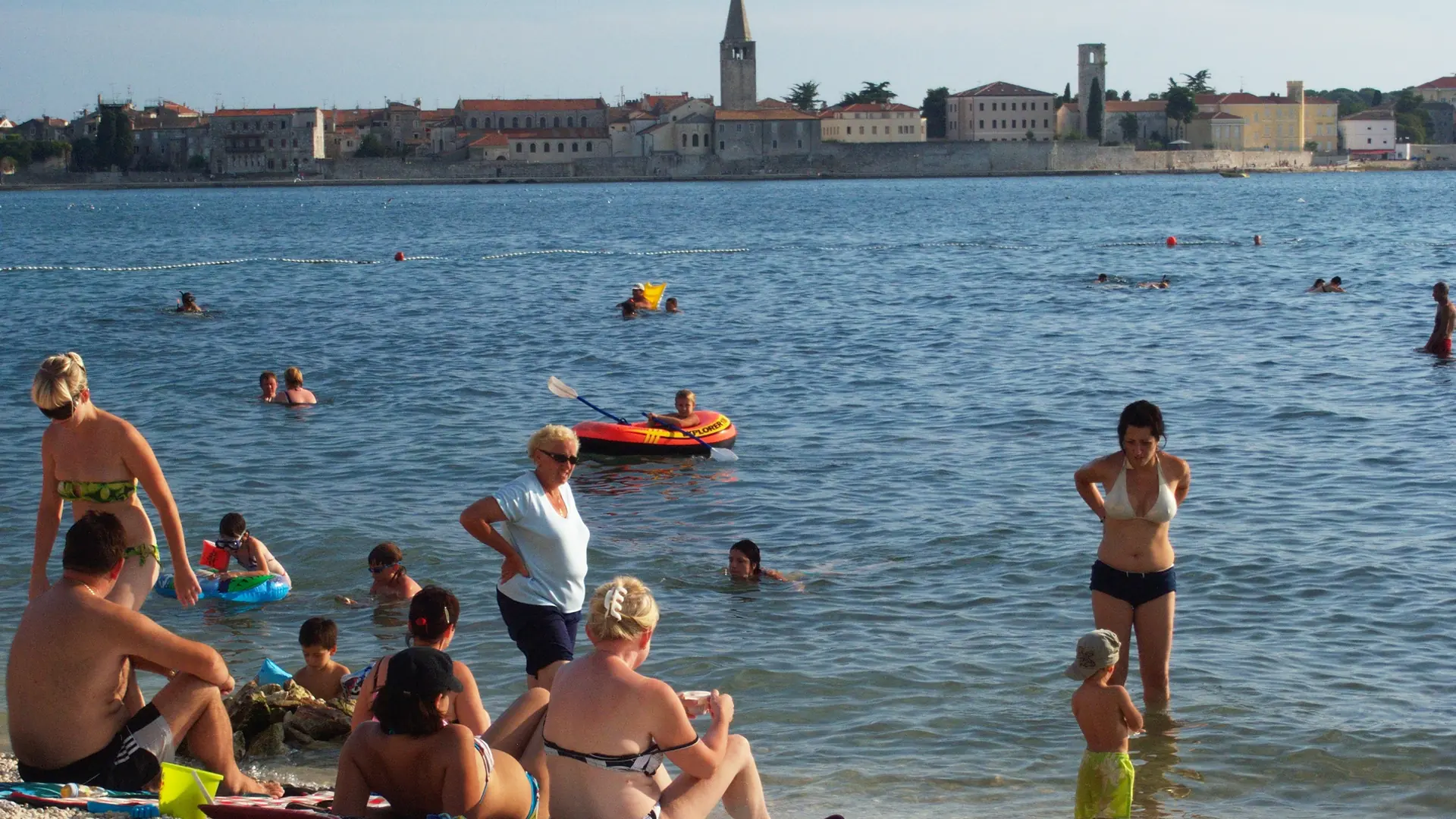 Swimmers at Borik Beach with Poreč Old Town and its basilica tower across the bay