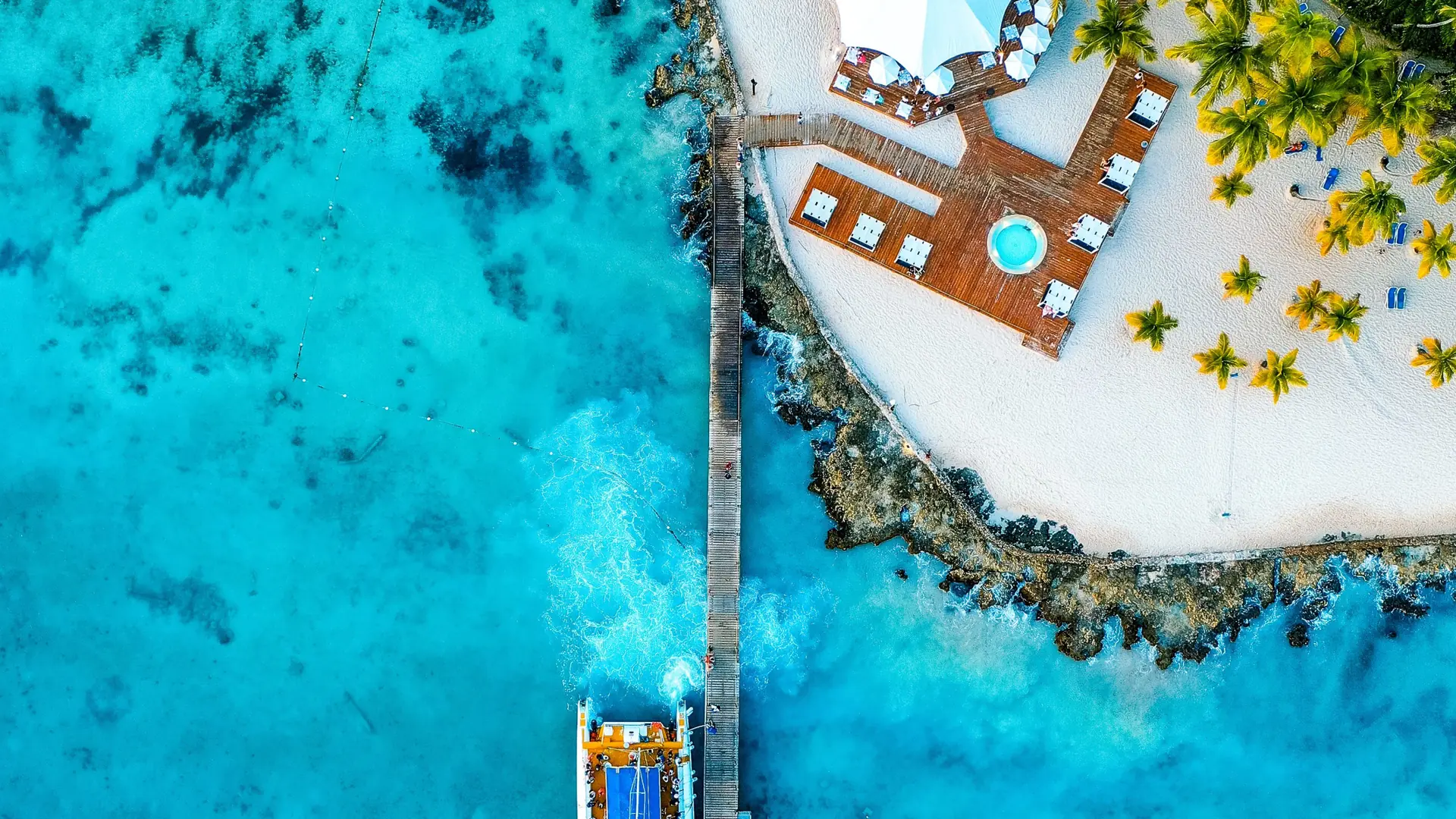 Aerial view of a sunny Bayahíbe beachfront pier, palms and bright blue water
