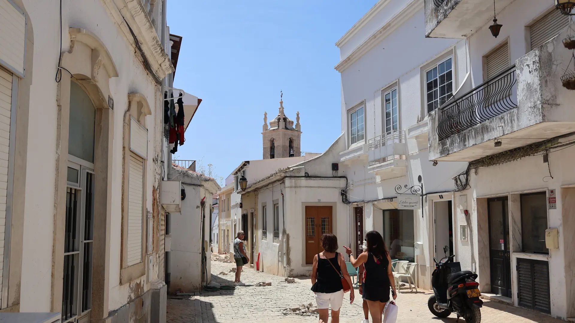a whitewashed lane in Lagos Old Town with a church bell tower ahead, bright sunlight