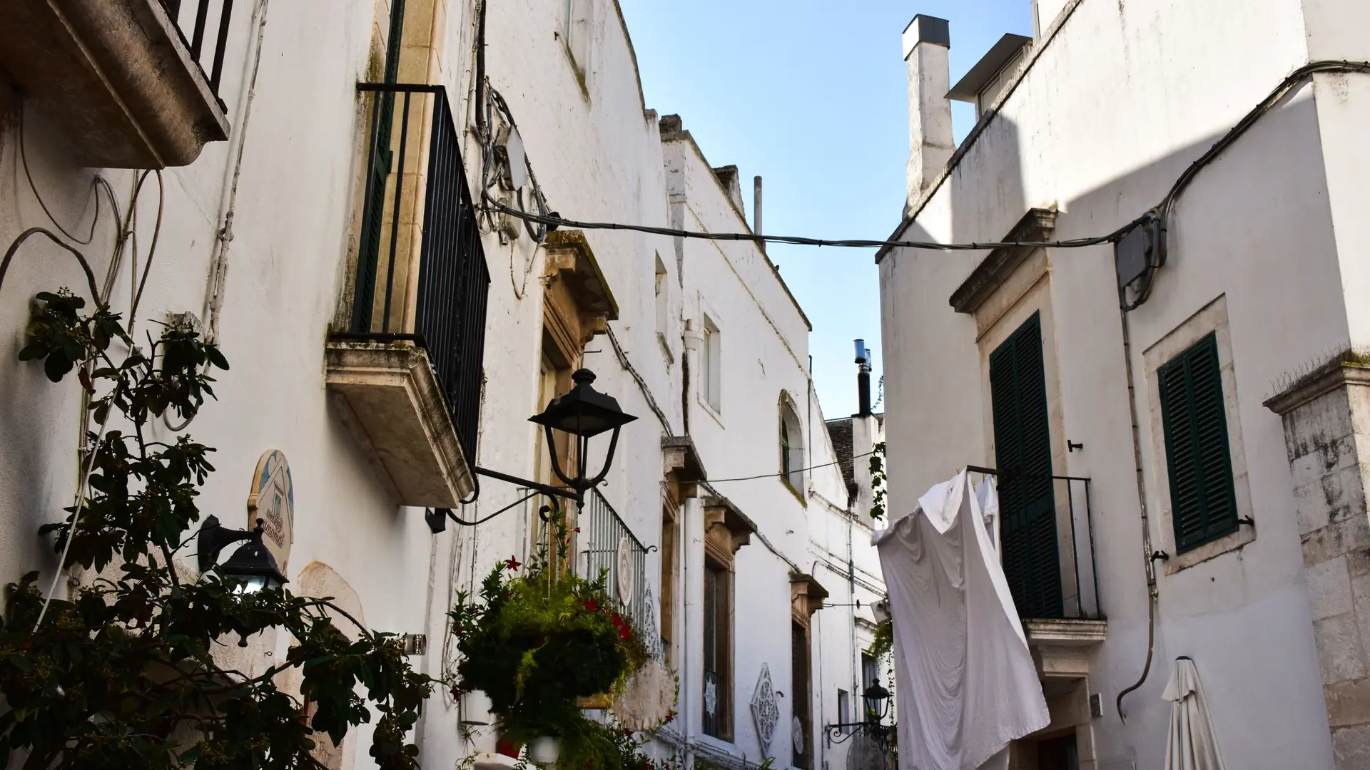 laundry hanging over a whitewashed Bari Vecchia lane under a clear blue sky