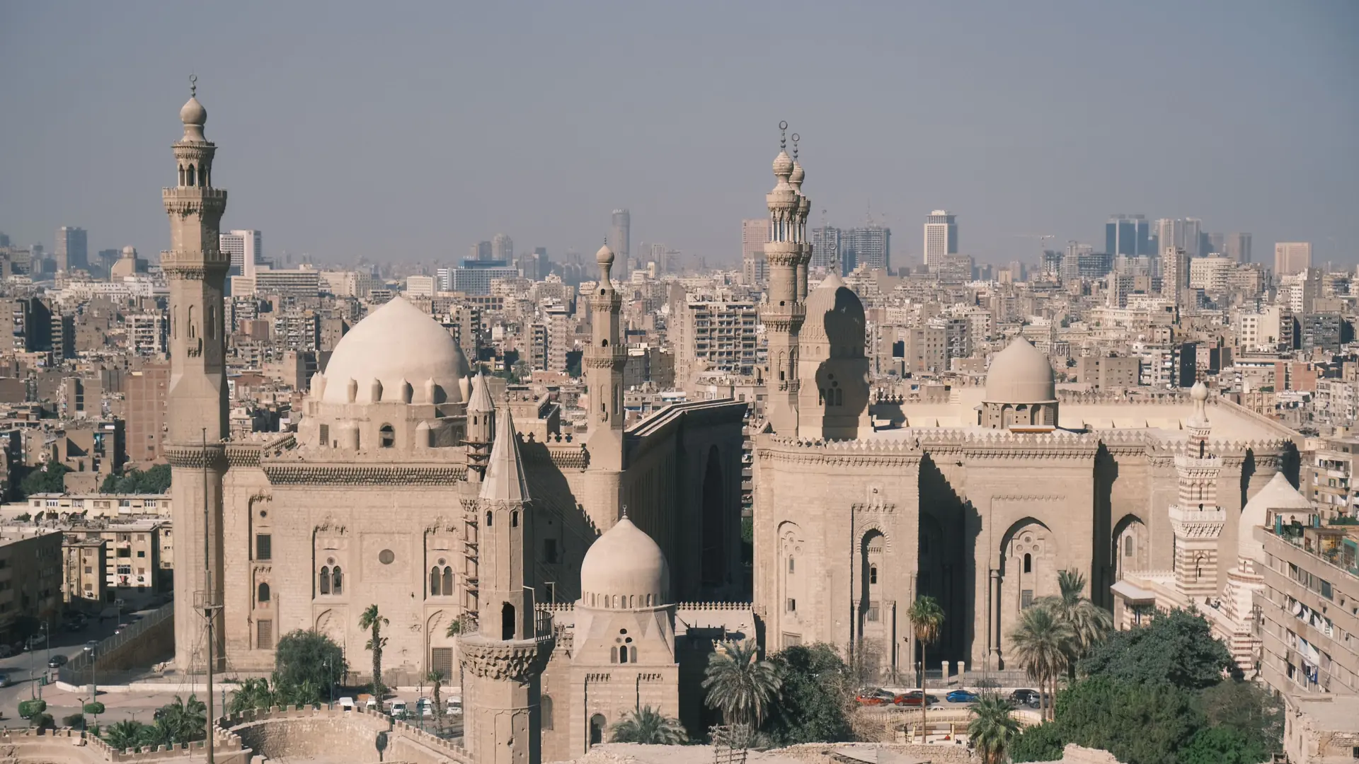 Historic mosque domes and minarets overlooking Cairo's sunlit city skyline.