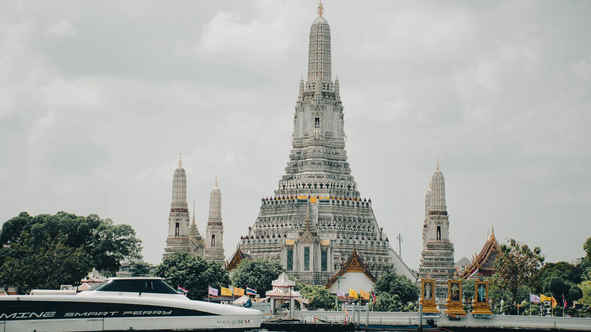 Wat Arun's porcelain spires above the Chao Phraya River under white clouds