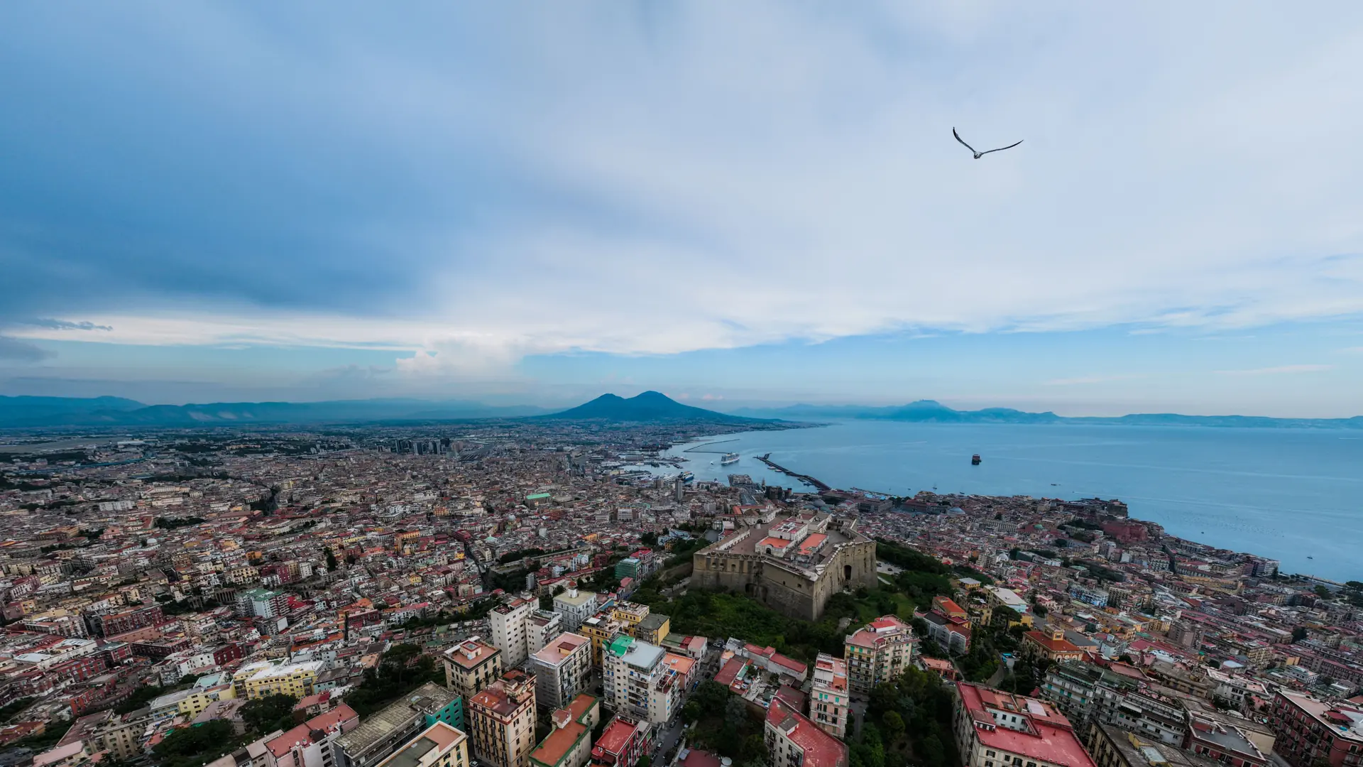 A sunlit view over Naples rooftops toward the bay and Mount Vesuvius