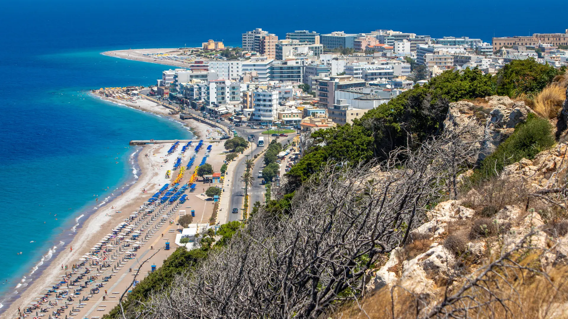 Rhodes Town’s coastline and beach below its modern waterfront buildings, shown as a wider island setting
