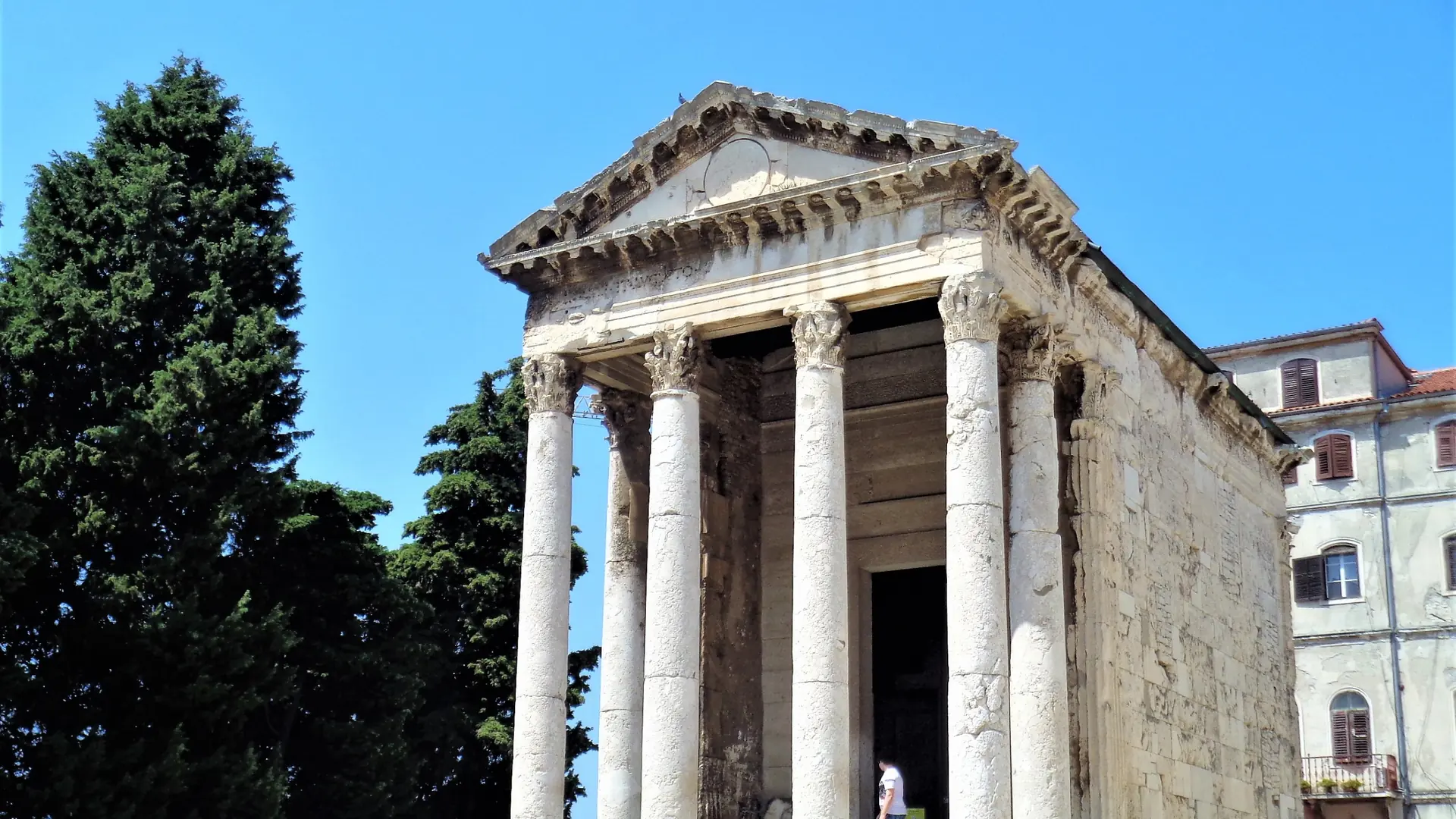 The Temple of Augustus's Corinthian columns under a clear blue sky in Pula's Forum