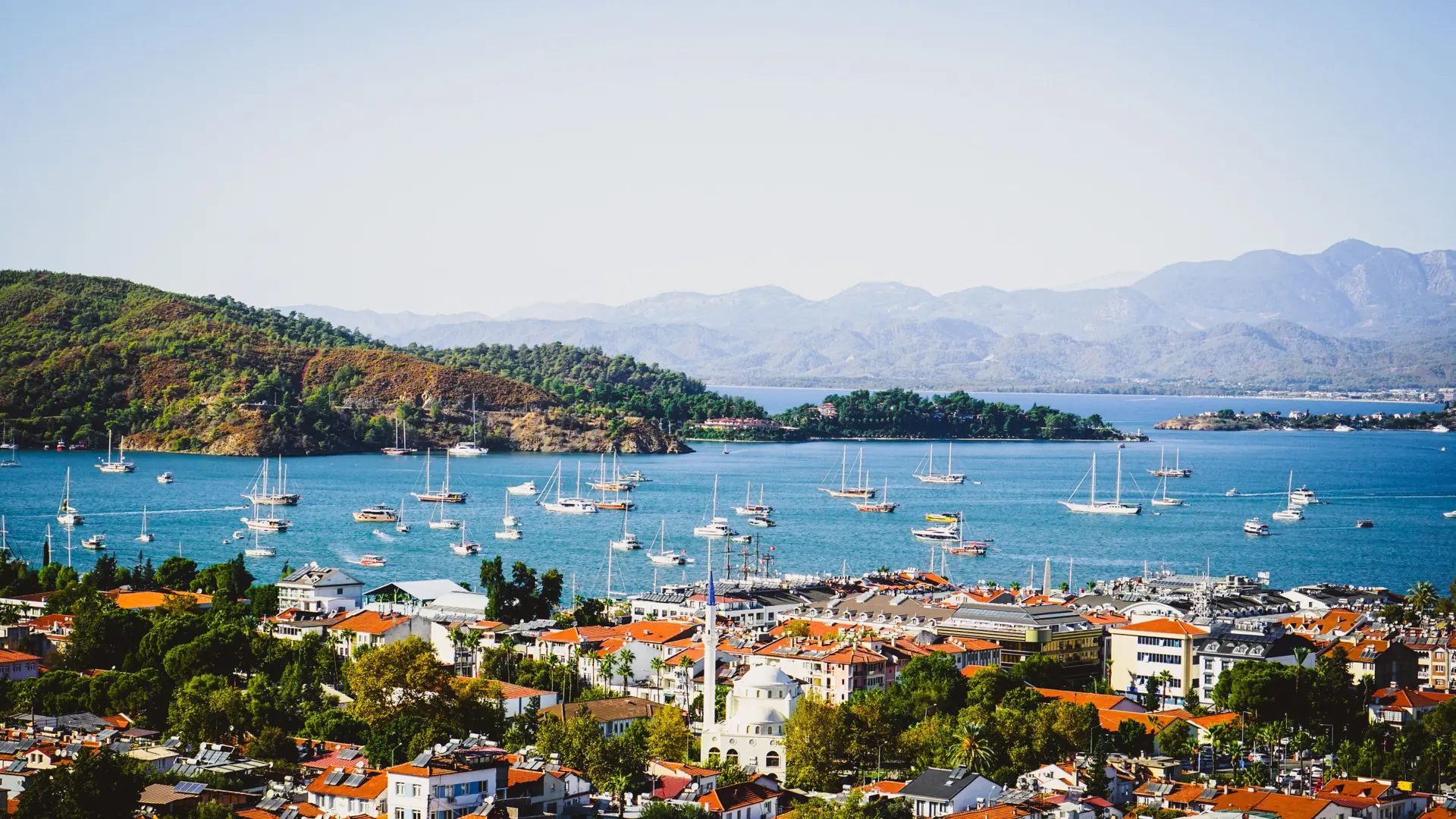 Sunny Fethiye harbour with sailing boats, waterfront buildings and green hills