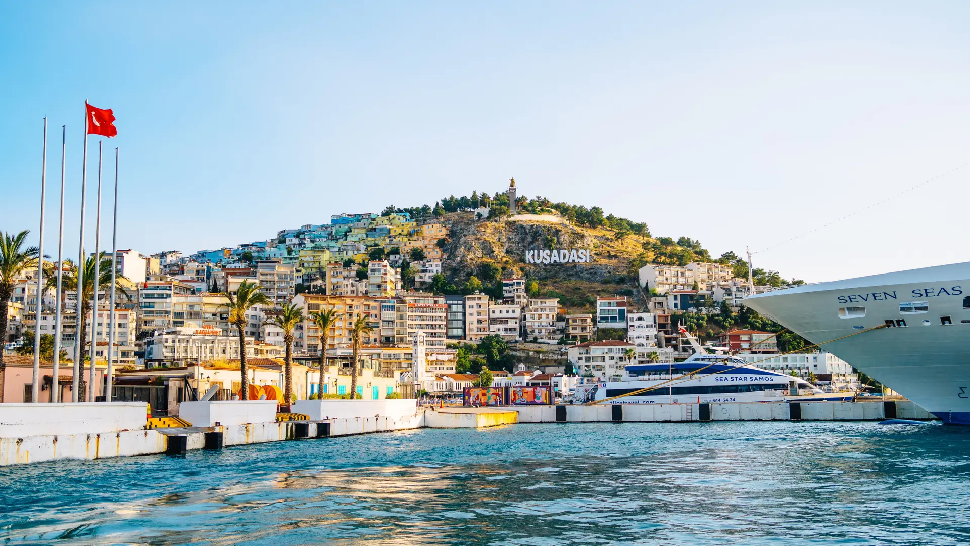 Cruise ships beside Kuşadası harbour with the hillside town lettering in bright daylight
