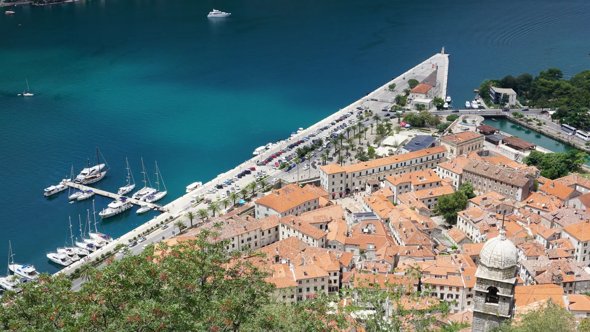 Aerial view of Kotor's Old Town roofs and marina beside the bay on a sunny day