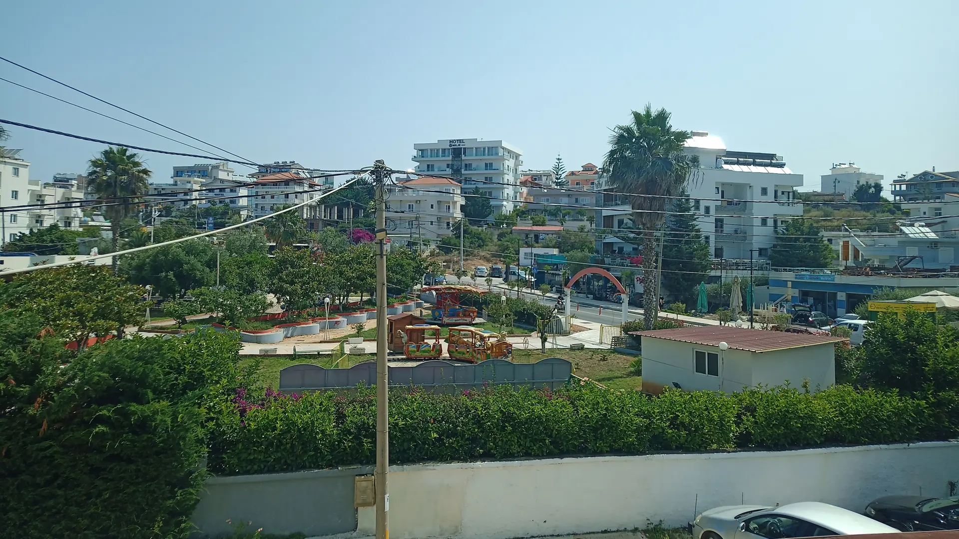 Houses, hotels and palms in the centre of Ksamil village, seen from Rruga Dea on a sunny day