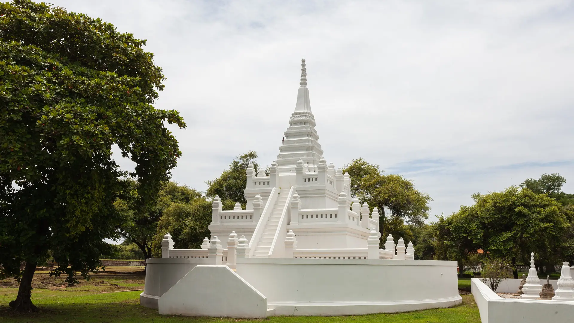 A sunlit Ayutthaya temple gateway and white chedi beyond it