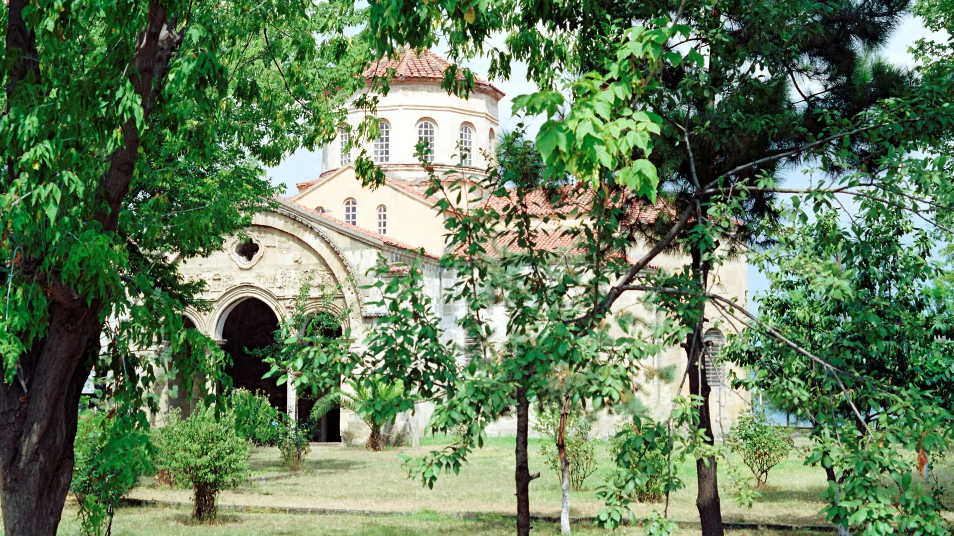 Hagia Sophia of Trabzon through sunlit garden trees in 1993, shown as a wider city scene