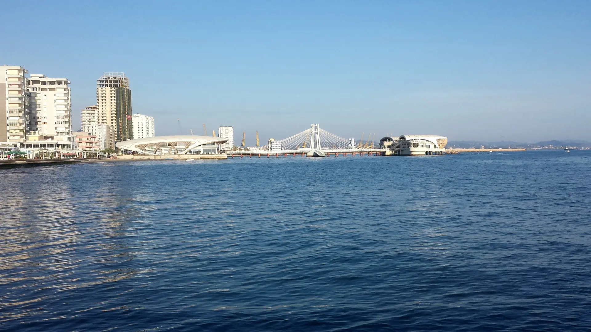 Seafront towers and the promenade pier of Durrës across calm blue water on a sunny day