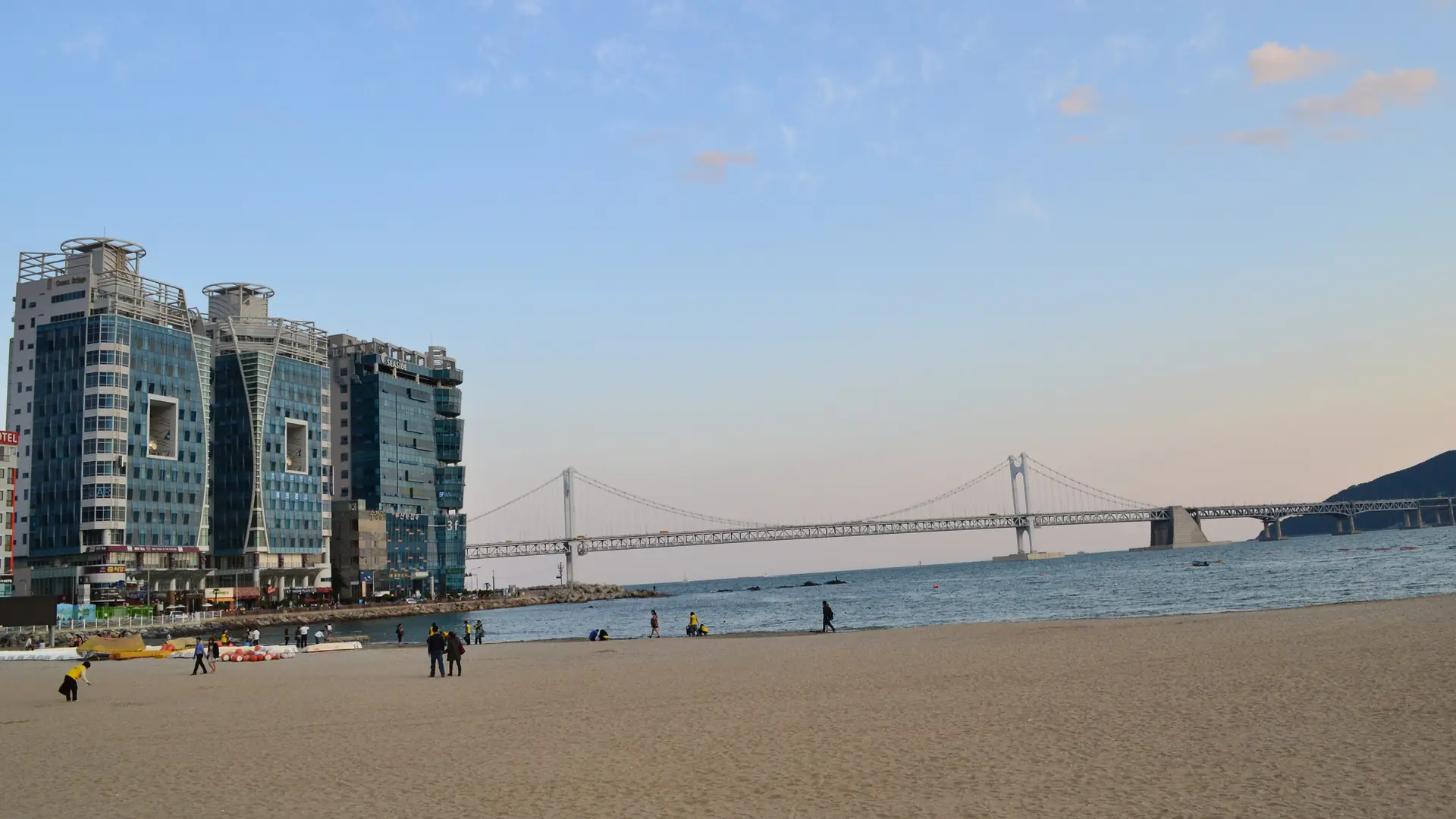 Gwangalli Beach's sand with the Gwangan Bridge stretching across the bay under a bright evening sky, Busan