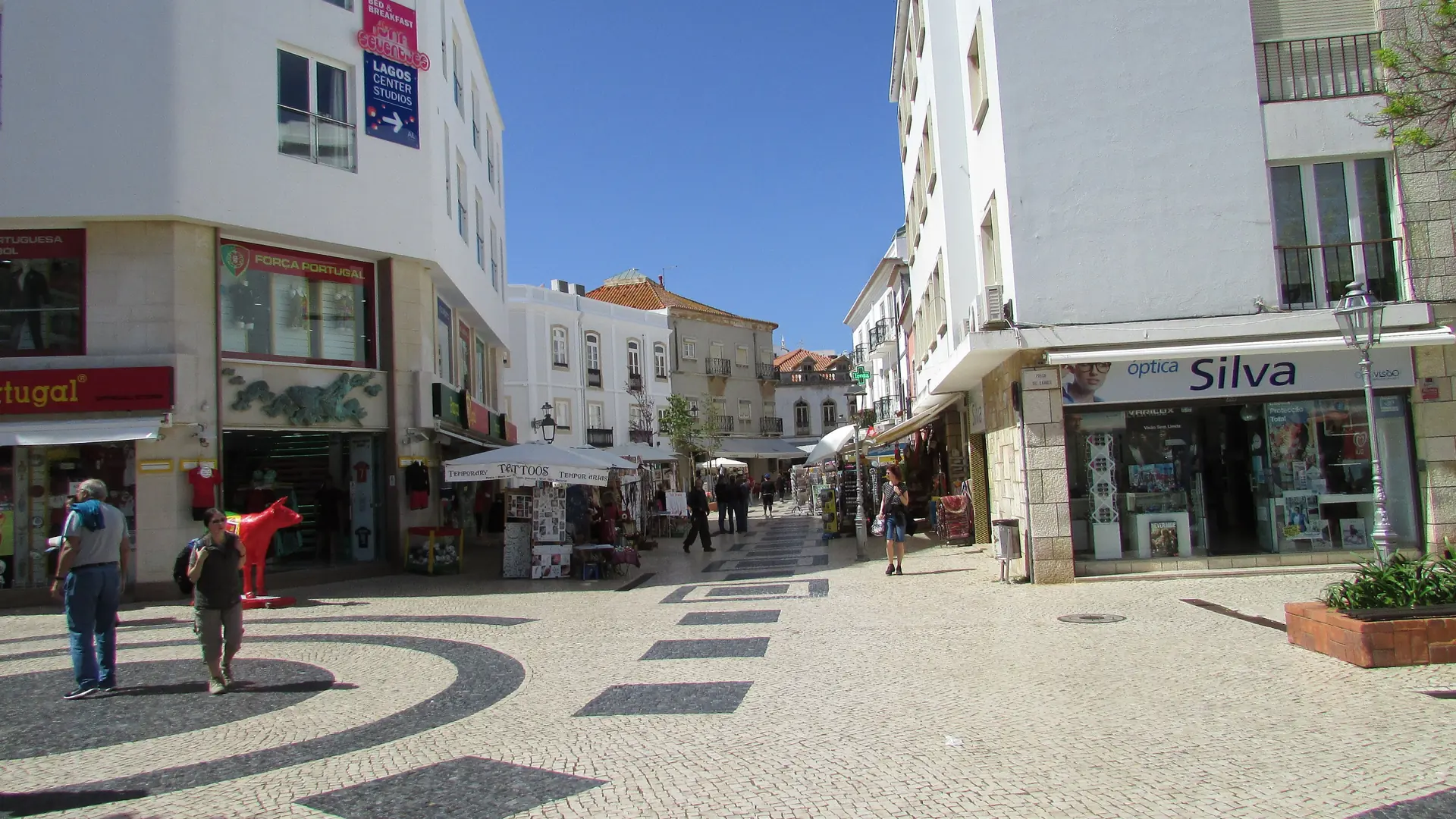 Sunny Rua Garrett seen from Praça Gil Eanes, with patterned paving and shops in Lagos