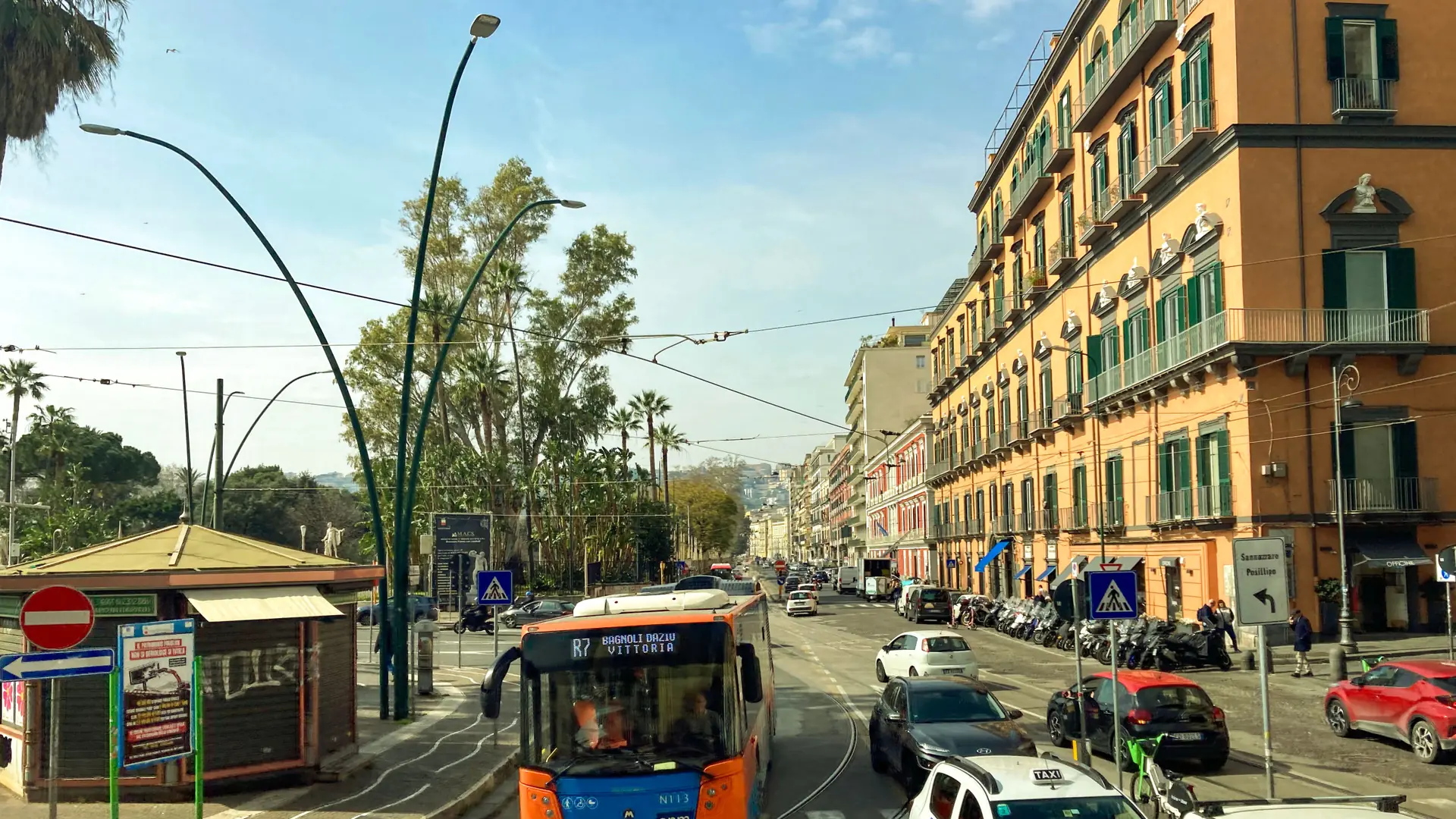 a palm-lined Naples street with a local bus and elegant facades under a bright sky
