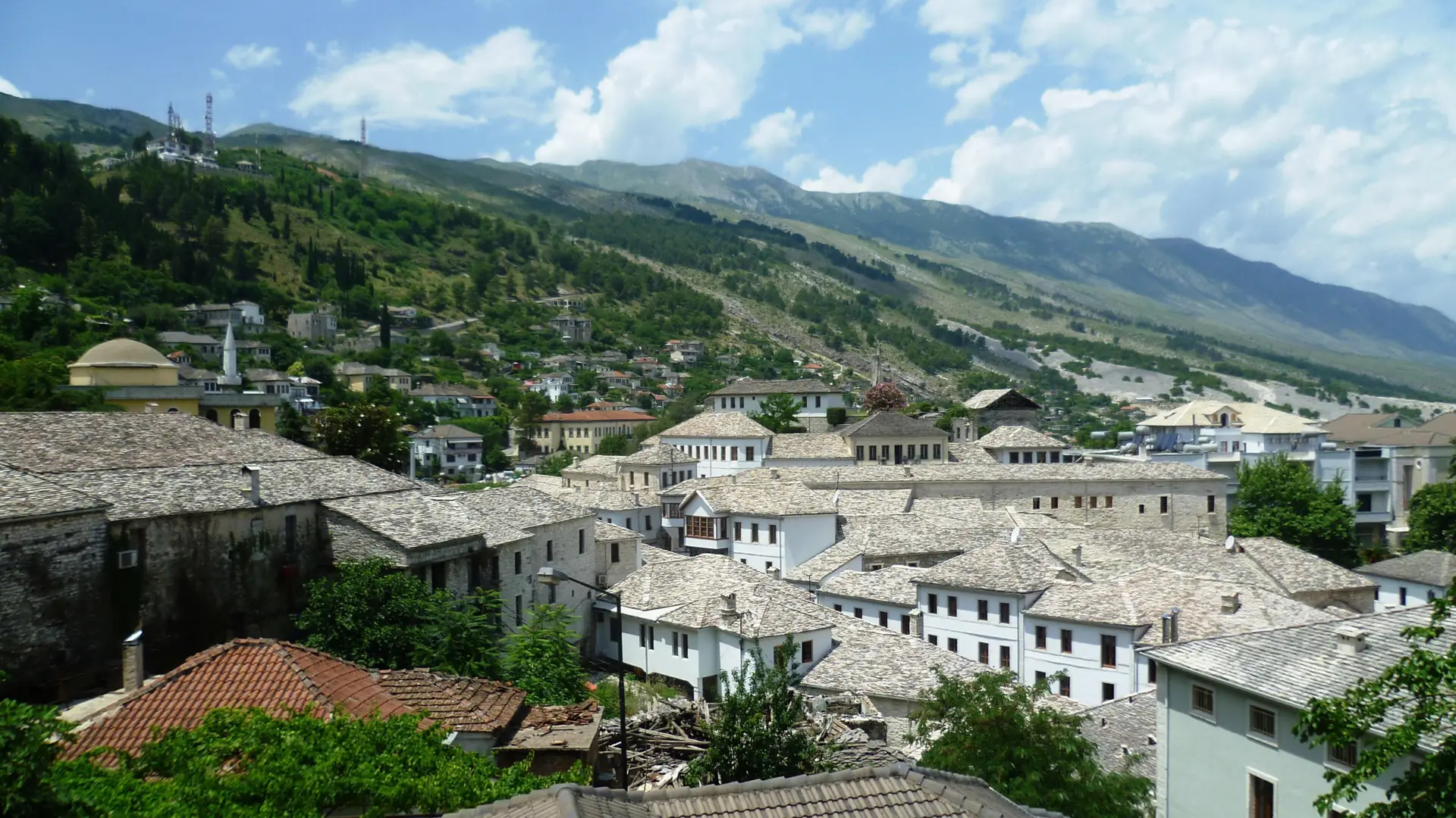 Grey stone roofs of Gjirokastër's old town below green mountains under a blue sky