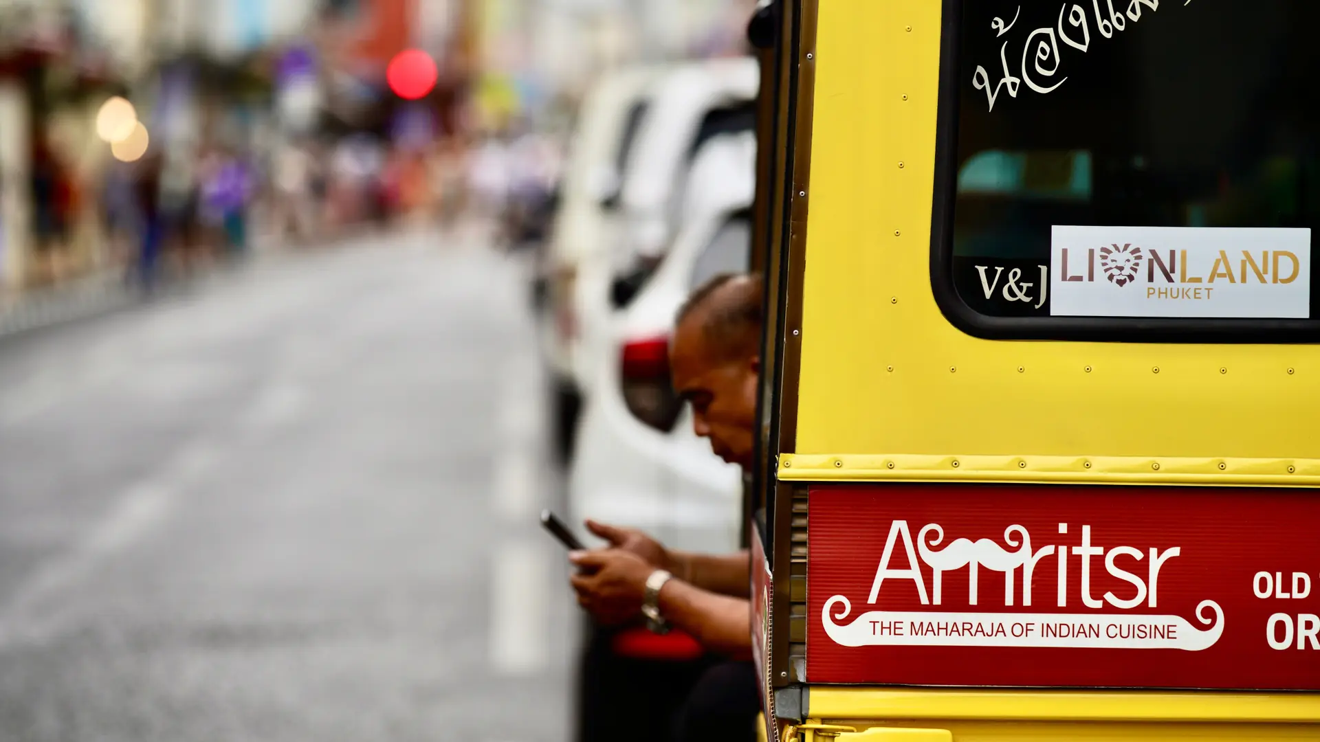 A colourful tuk-tuk moving through a lively Phuket street