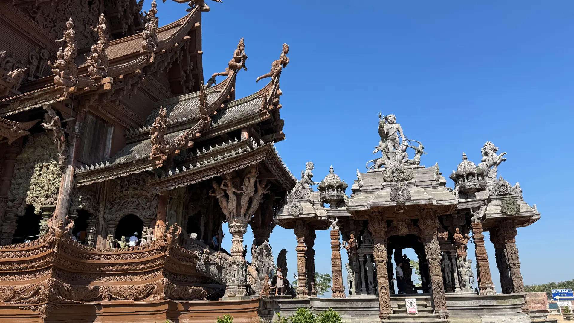 Carved wooden roofs and figures at the Sanctuary of Truth in Pattaya under a clear blue sky
