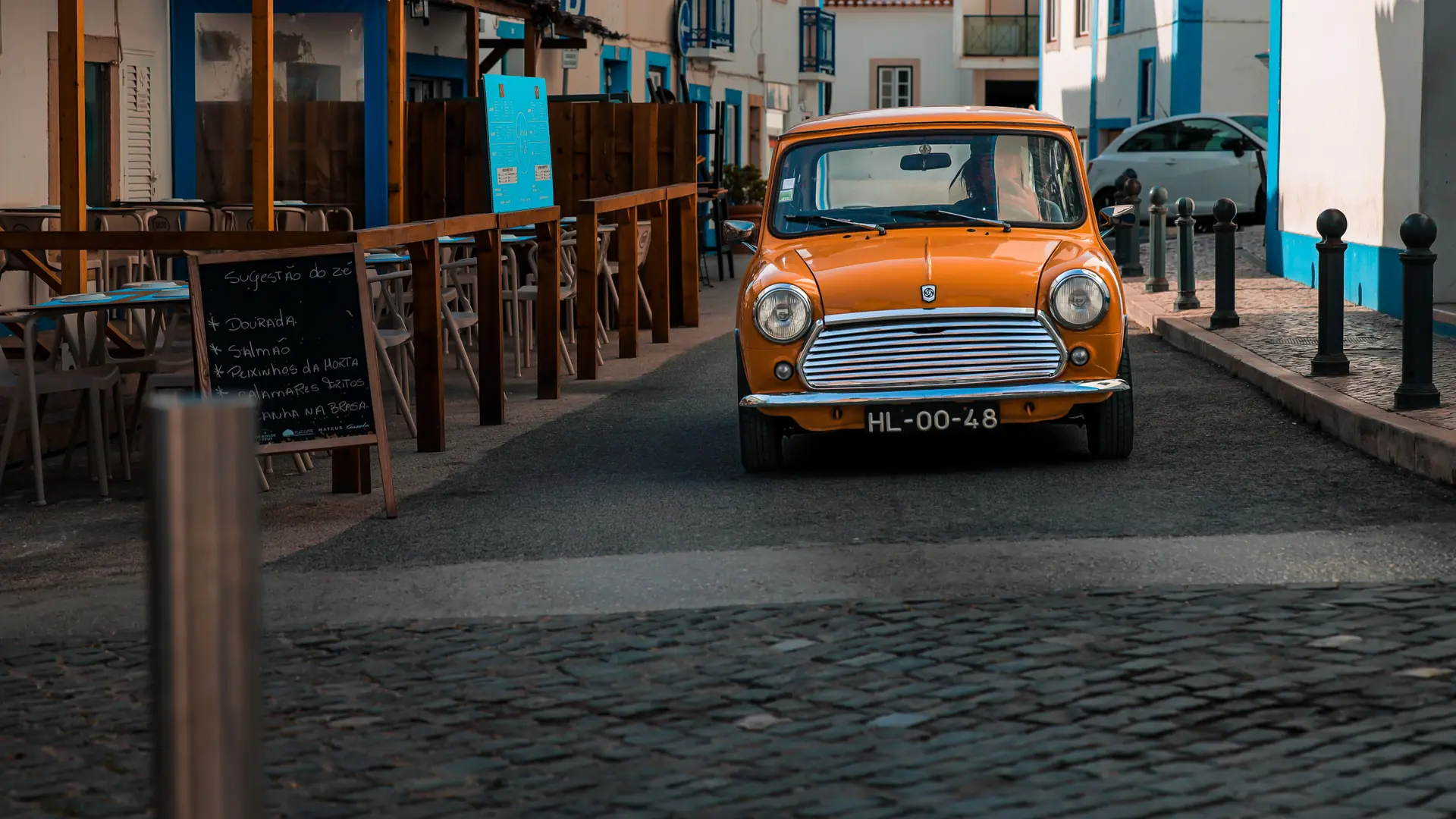 a sunny Albufeira old town street with café tables, a vintage car and colourful façades